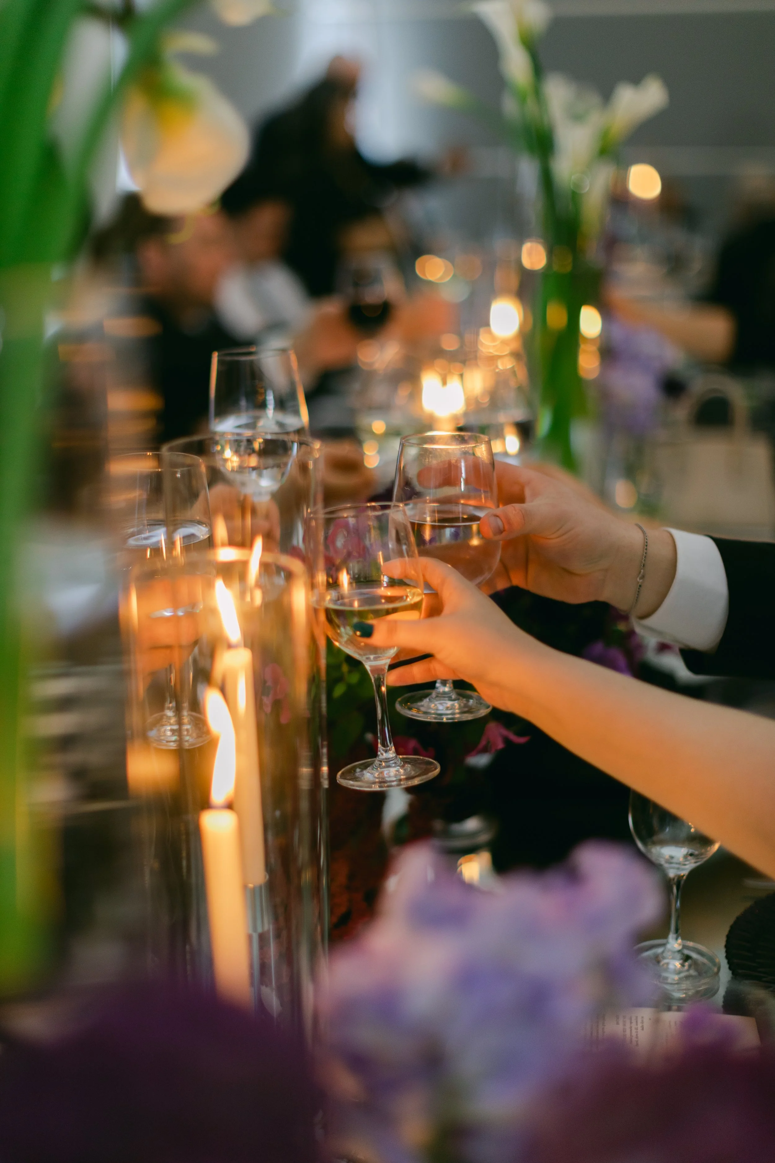 People celebrating with wine glasses at a dinner event, with candles and flowers on the table, in an elegant setting.