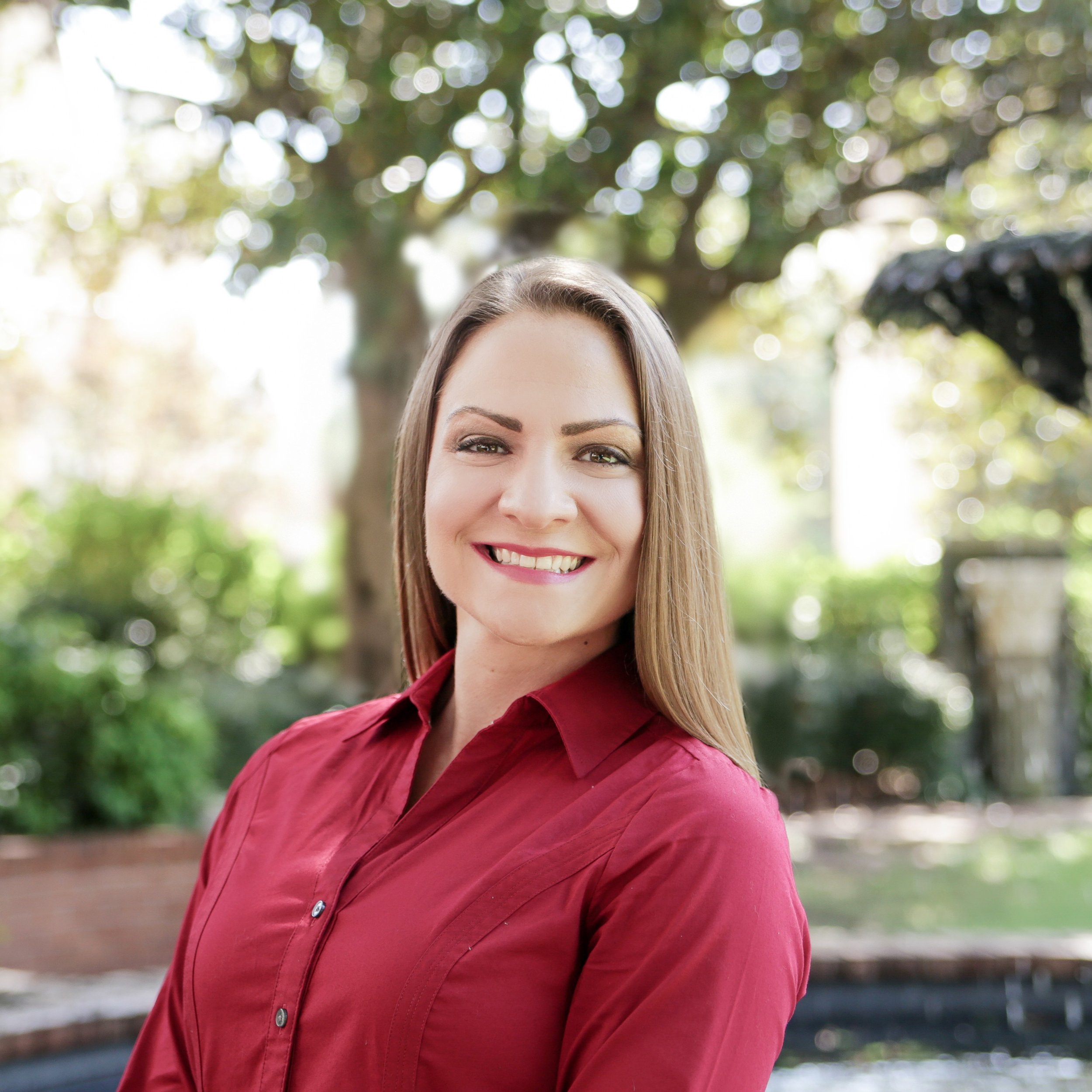 Stephanie is wearing a red button-down shirt and smiling while standing outside.