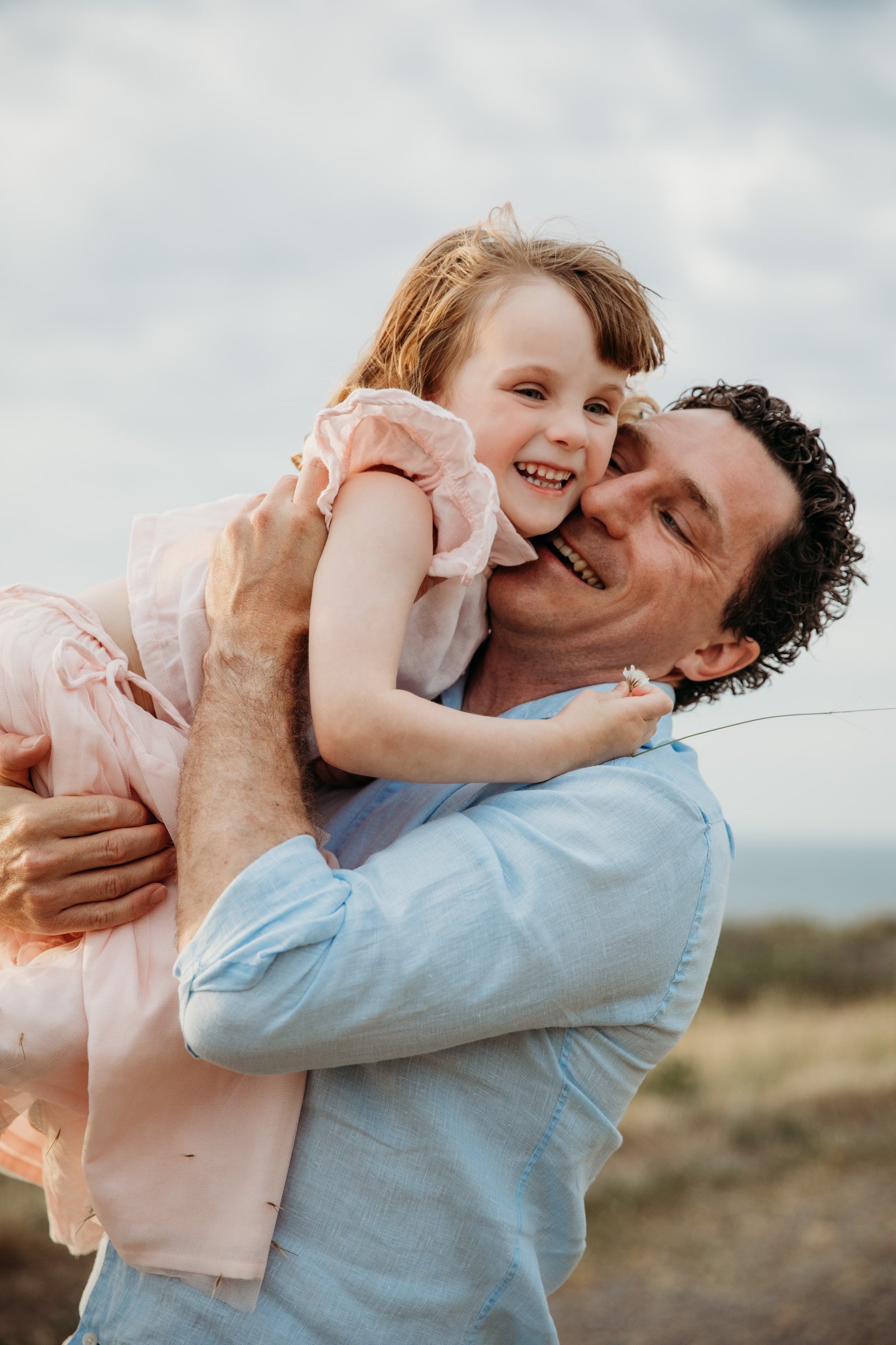 Dad lifts up his daughter in a happy embrace outdoors during a natural family photography session