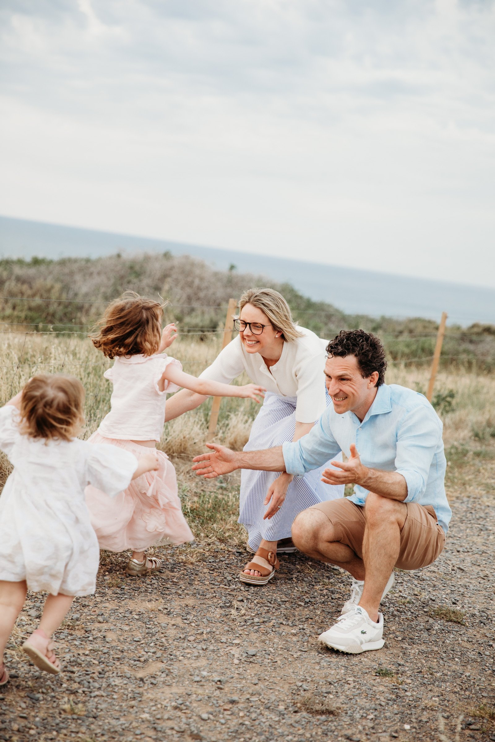 Two young sisters run into their parents' open arms during a natural outdoor family photography session.