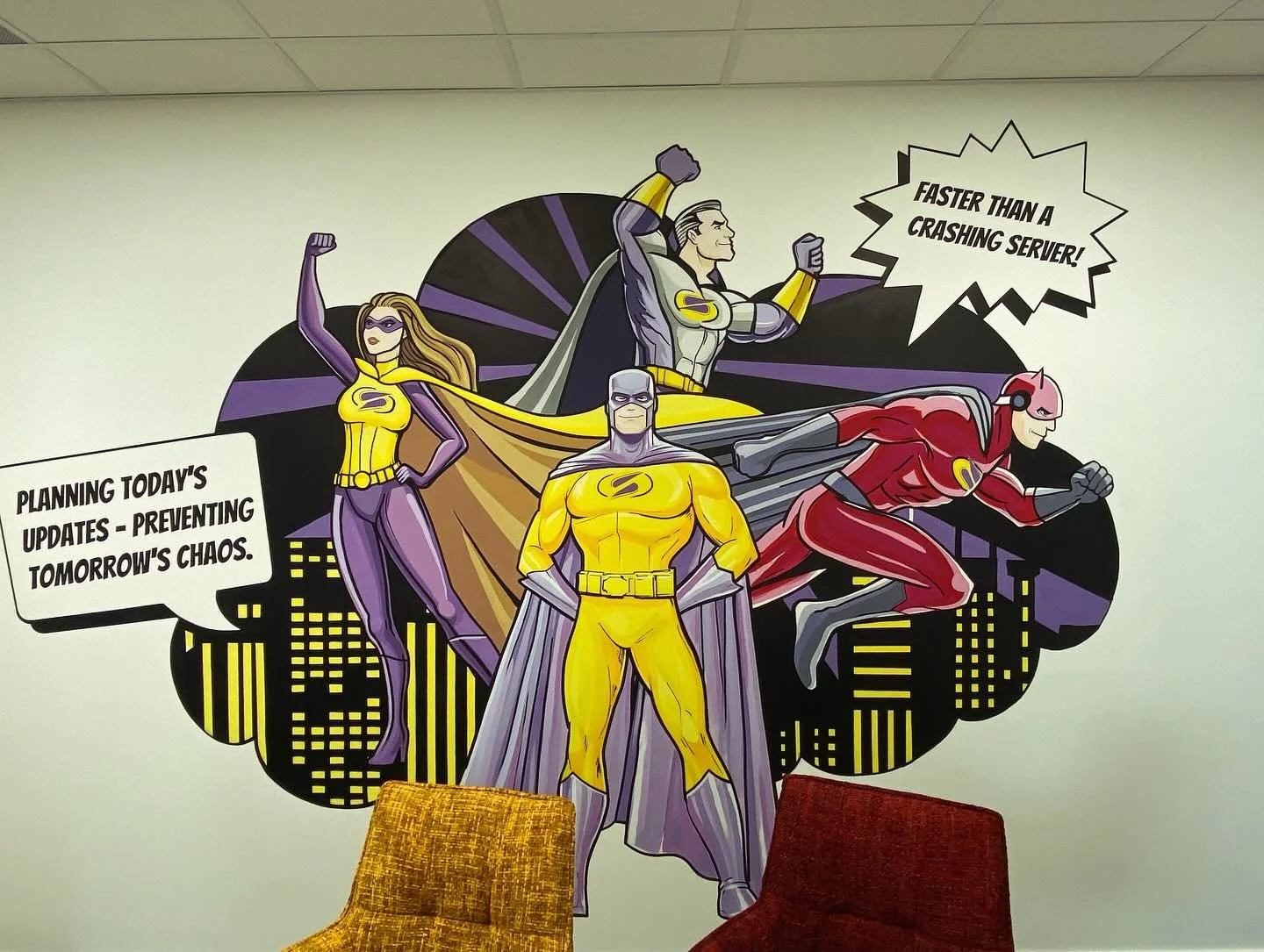 Decorative wall art featuring comic book superheroes planning with speech bubbles. One confirms 'Faster than a crashing server!' and another says 'Planning today's updates - preventing tomorrow's chaos.' The superheroes include a woman in purple and 
