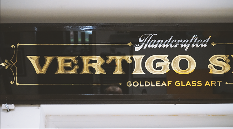 Sign for Vertigo, handcrafted glass art, with gold and black design.