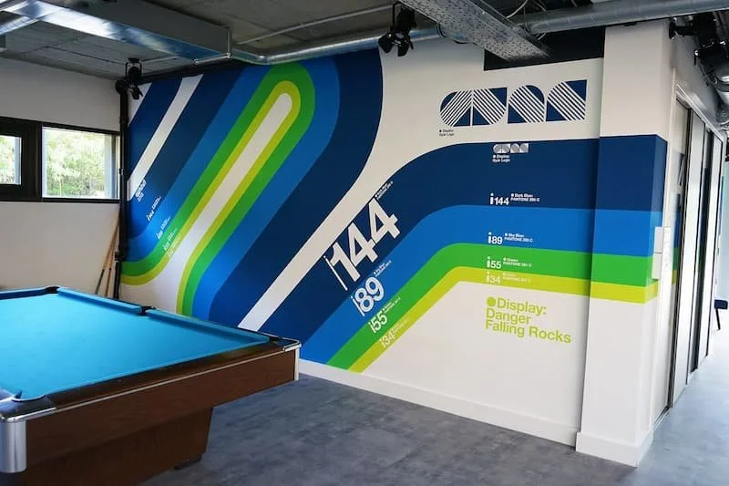 Interior of a room with a pool table and striped wall art showing athletic statistics and a warning about falling rocks.