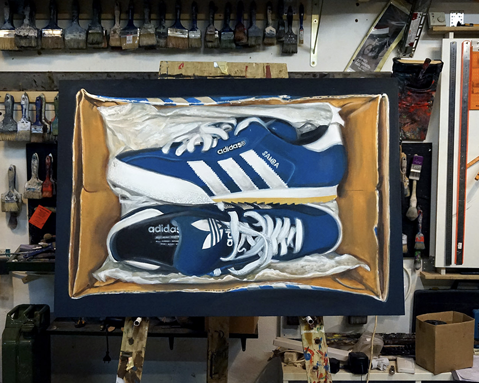 Painting of blue Adidas sneakers with white stripes inside a shoebox, on a workbench in a workshop.