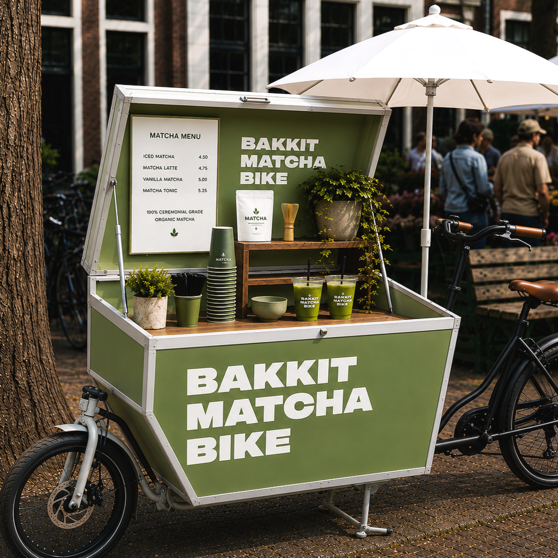 Een groene foodtruck genaamd 'Bakkit Matcha Bike' verkoopt matcha-drankjes, geplaatst op een straat met mensen op de achtergrond.