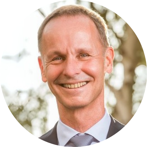 Ein Mann lächelnd bei Tageslicht, im Freien vor Bäumen