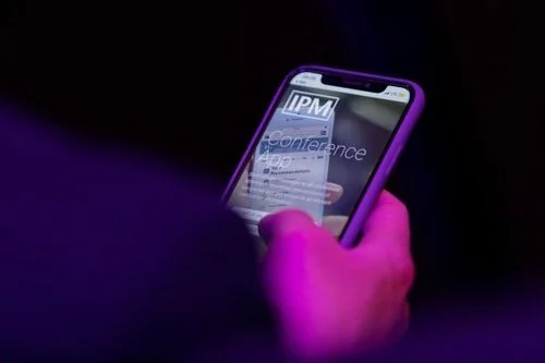 Nahaufnahme eines Handys mit einer App auf dem Bildschirm, die IPM Conference anzeigt.