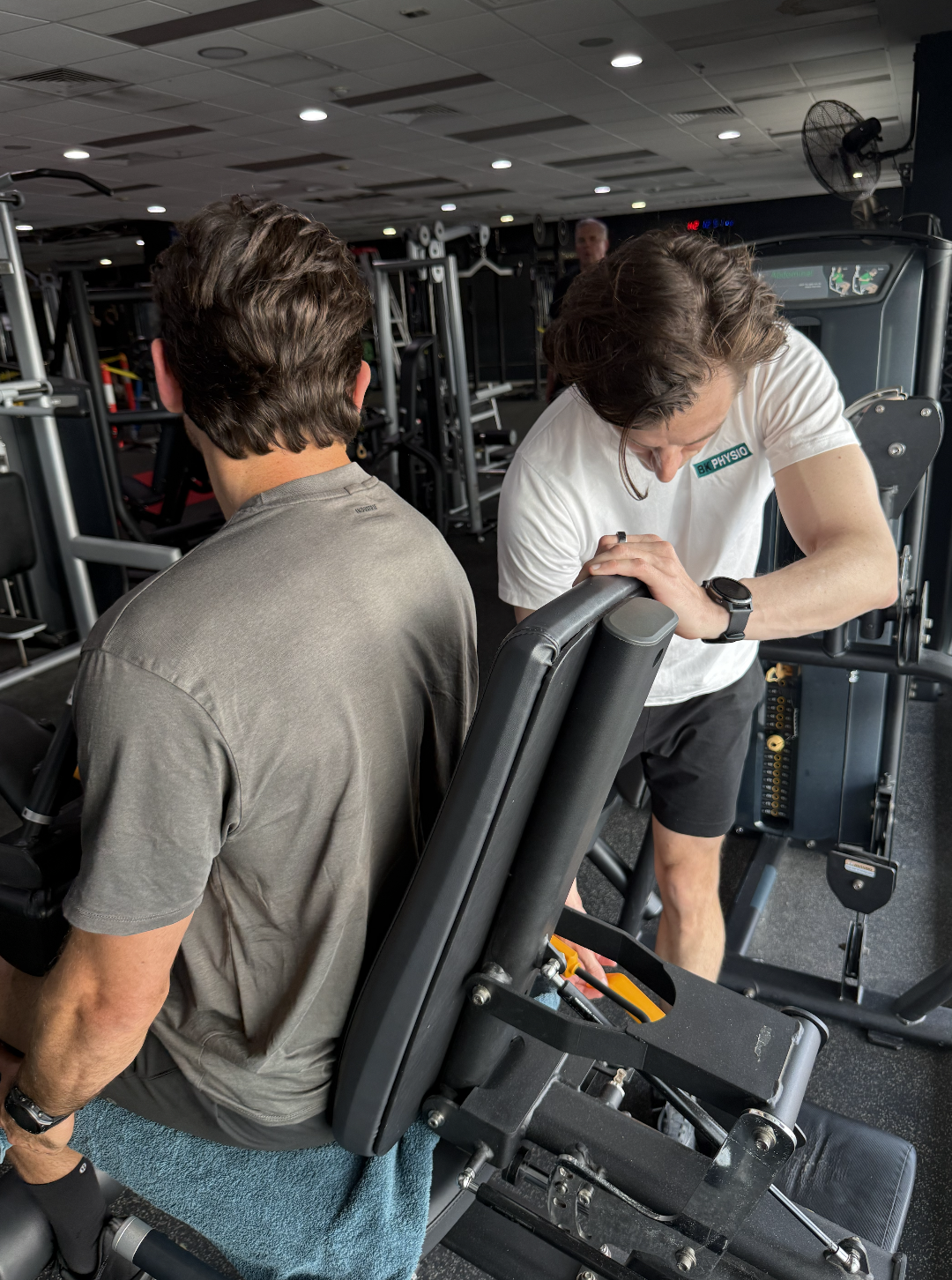 B K Physio physiotherapist adjusts some gym equipment for a client in the gym.