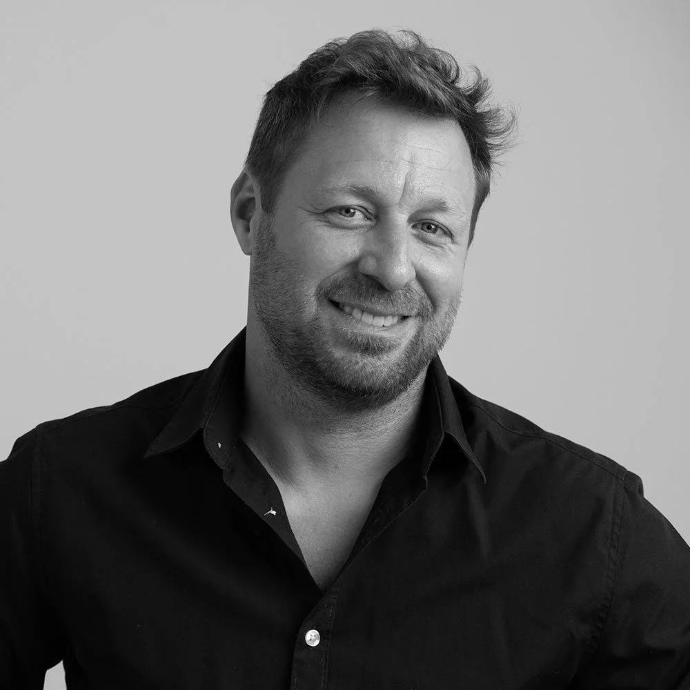 Black and white portrait of a man with short hair and a beard, smiling and wearing a collared shirt.