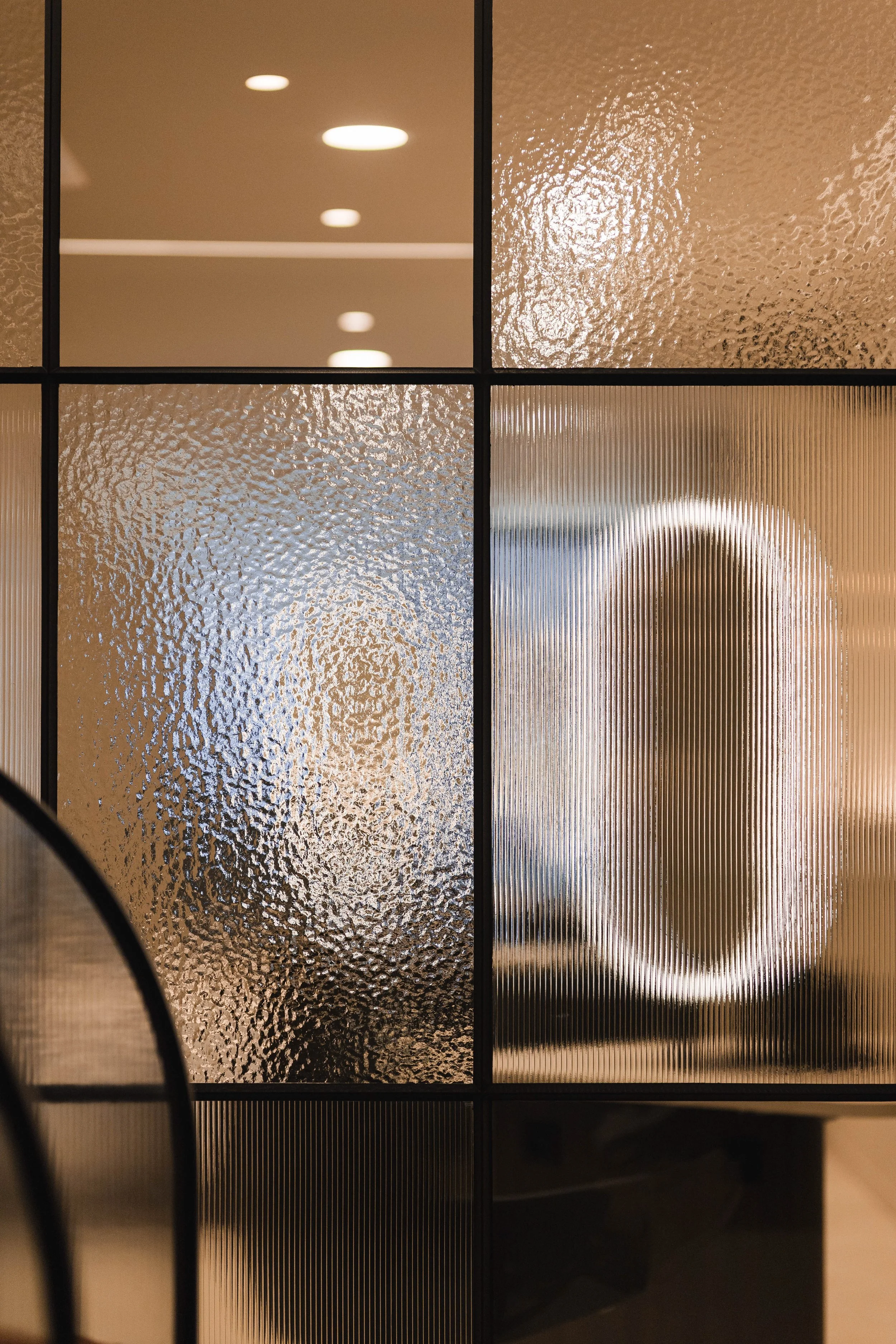 Glaswand met vier panelen, waarvan twee met geperforeerd en getextureerd glas, en twee met geribbeld glas, in een modern interieur.