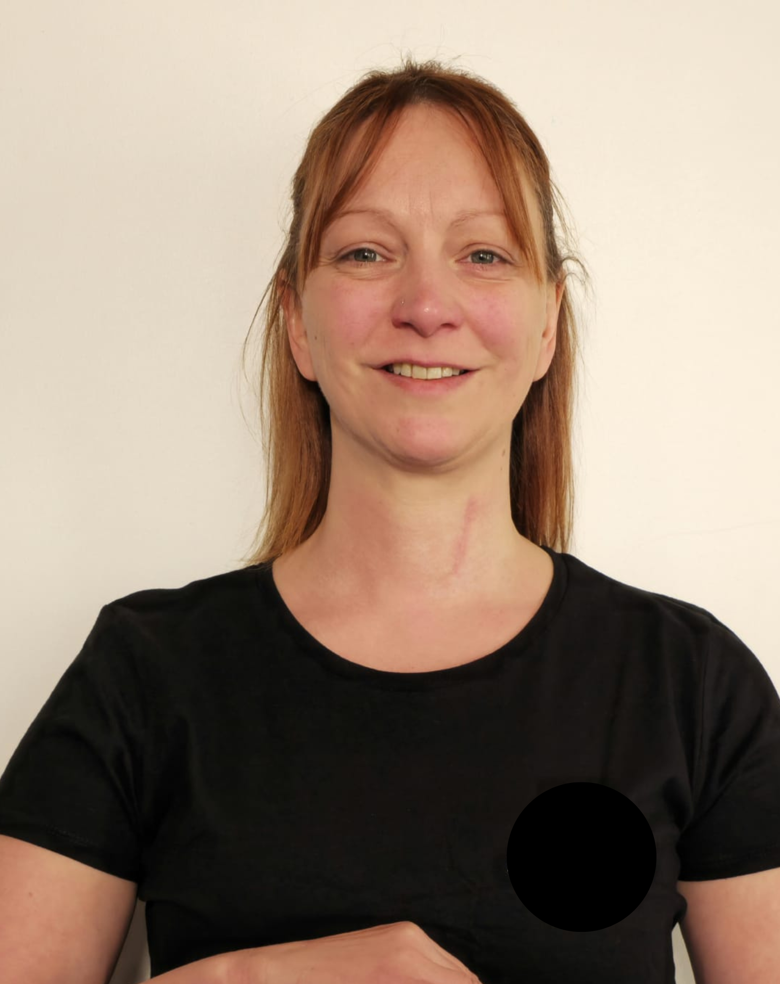 Portrait d'une femme souriante avec des cheveux bruns, portant un t-shirt noir,  en arrière-plan blanc.