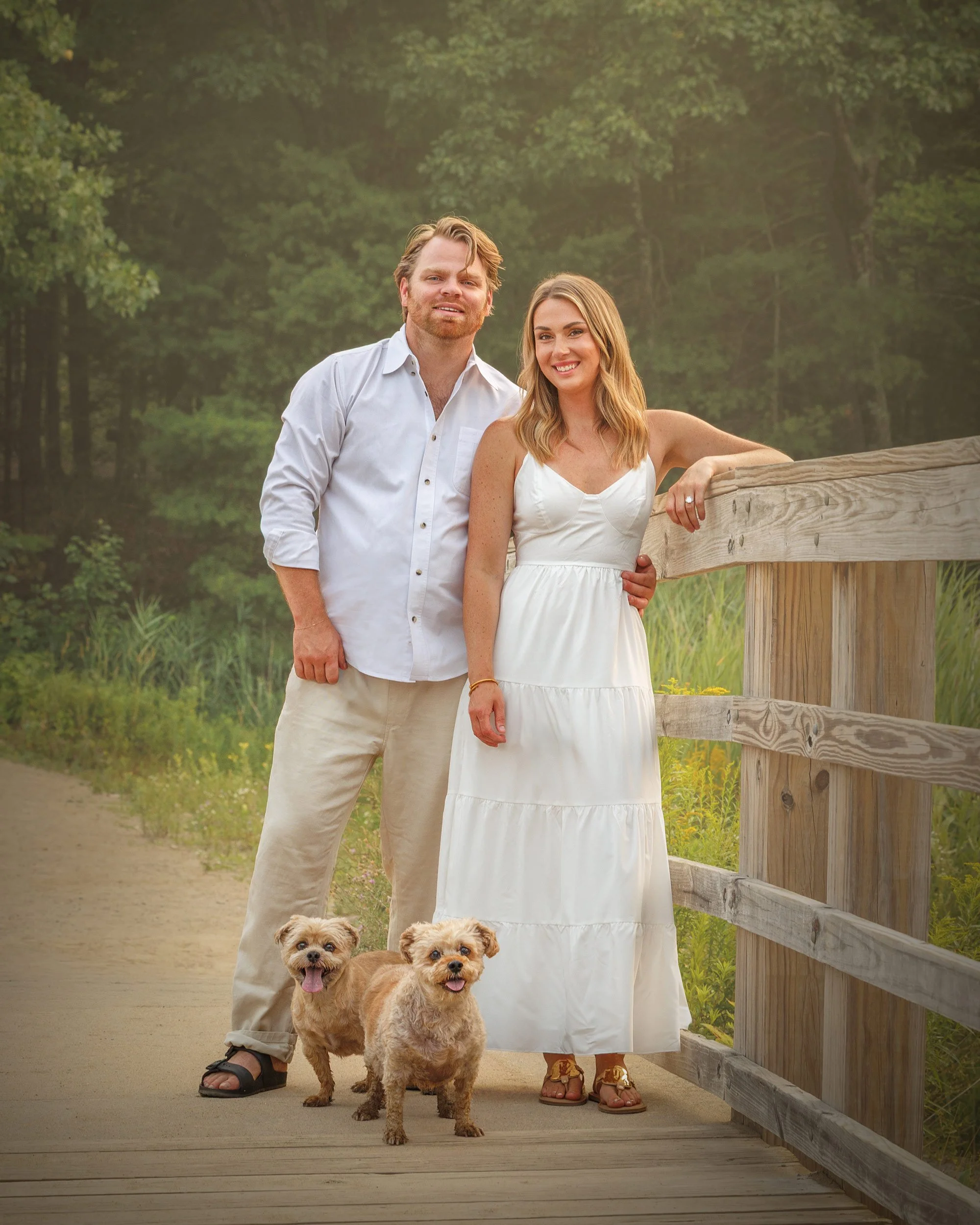 Fine art pet photography session featuring a smiling couple with their small dogs on a wooded path in Saratoga Springs NY