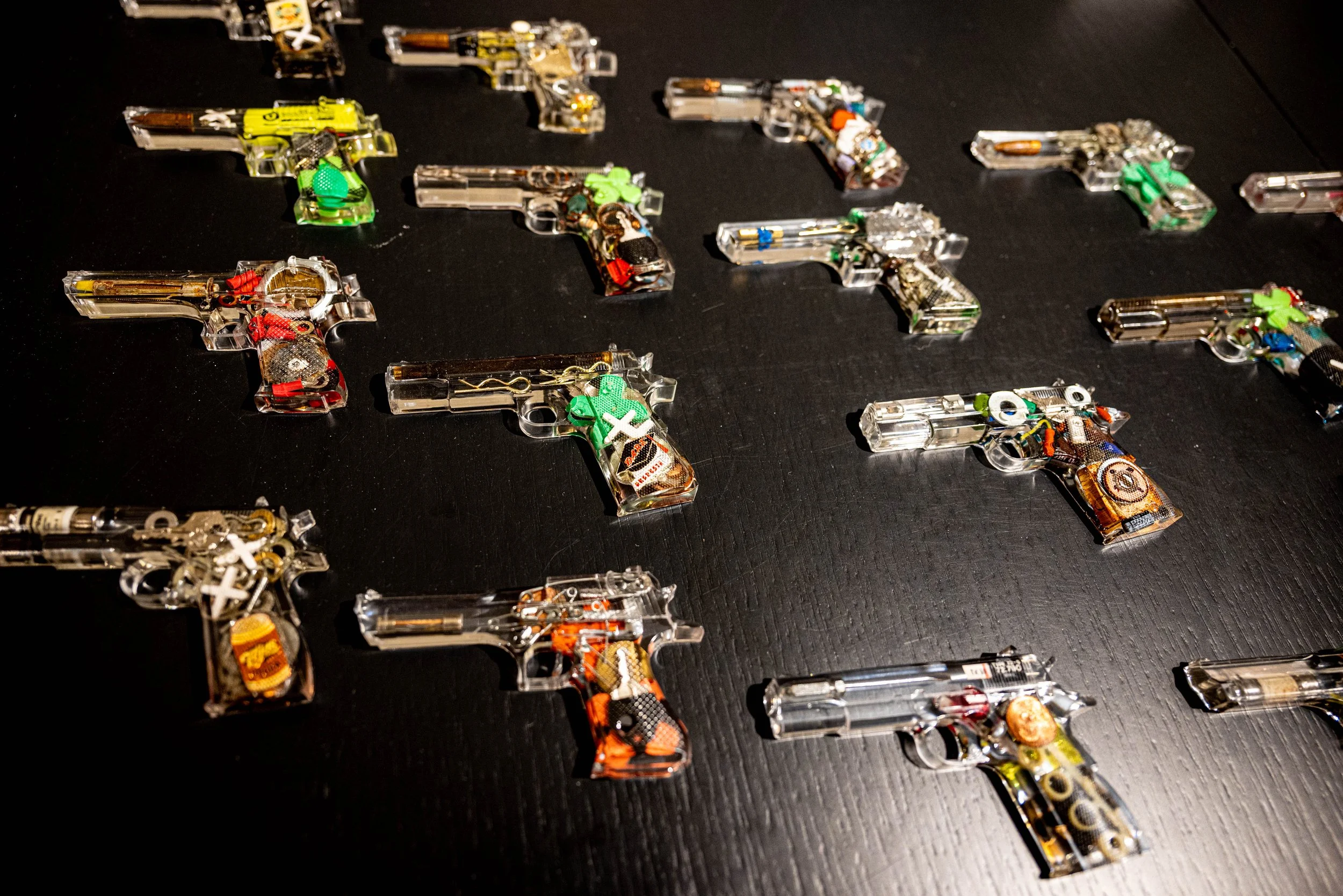 Multiple small, colorful, transparent keychain guns arranged on a black surface.