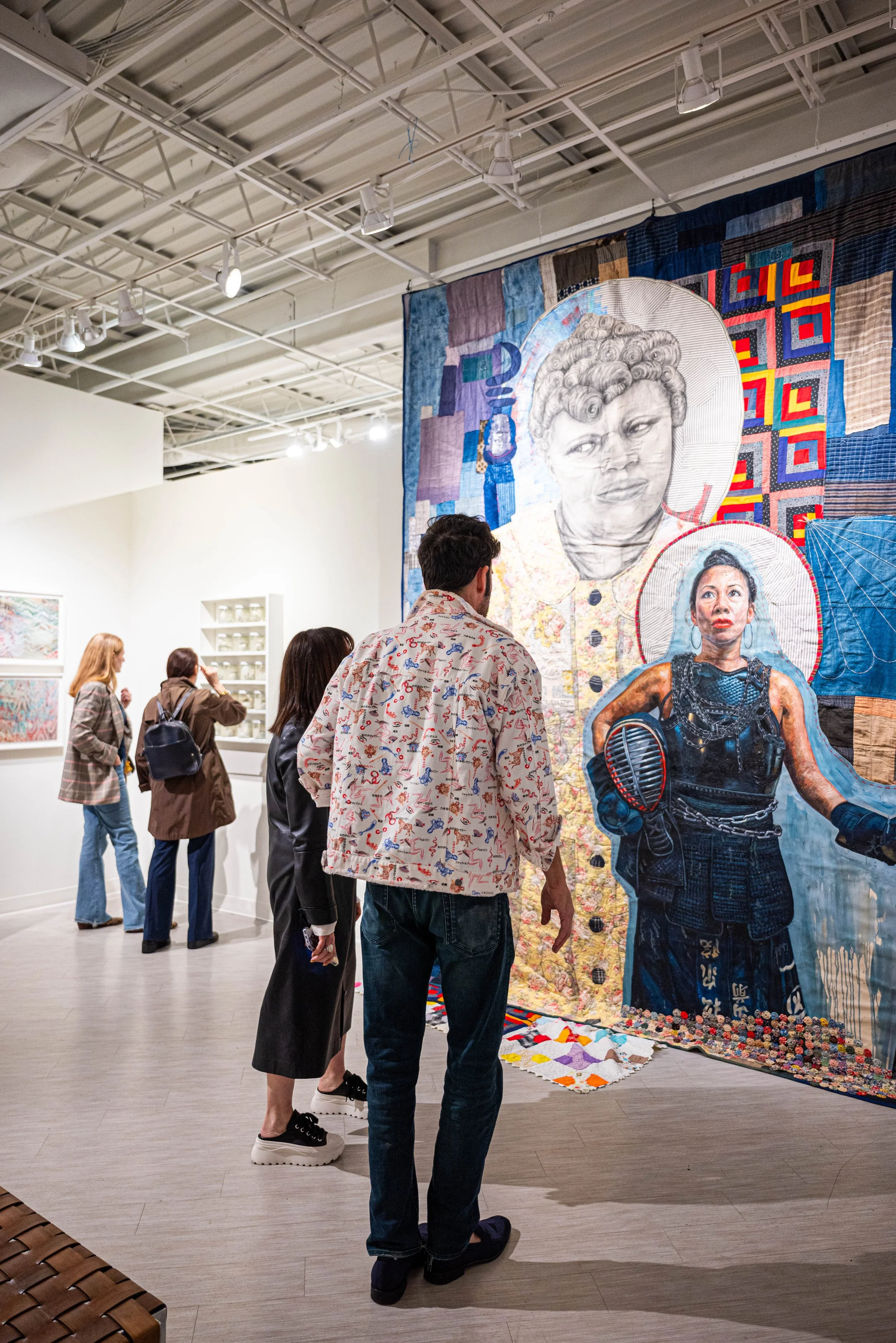People viewing a large textile artwork with detailed portraits of two women about to be exhibited in a gallery.