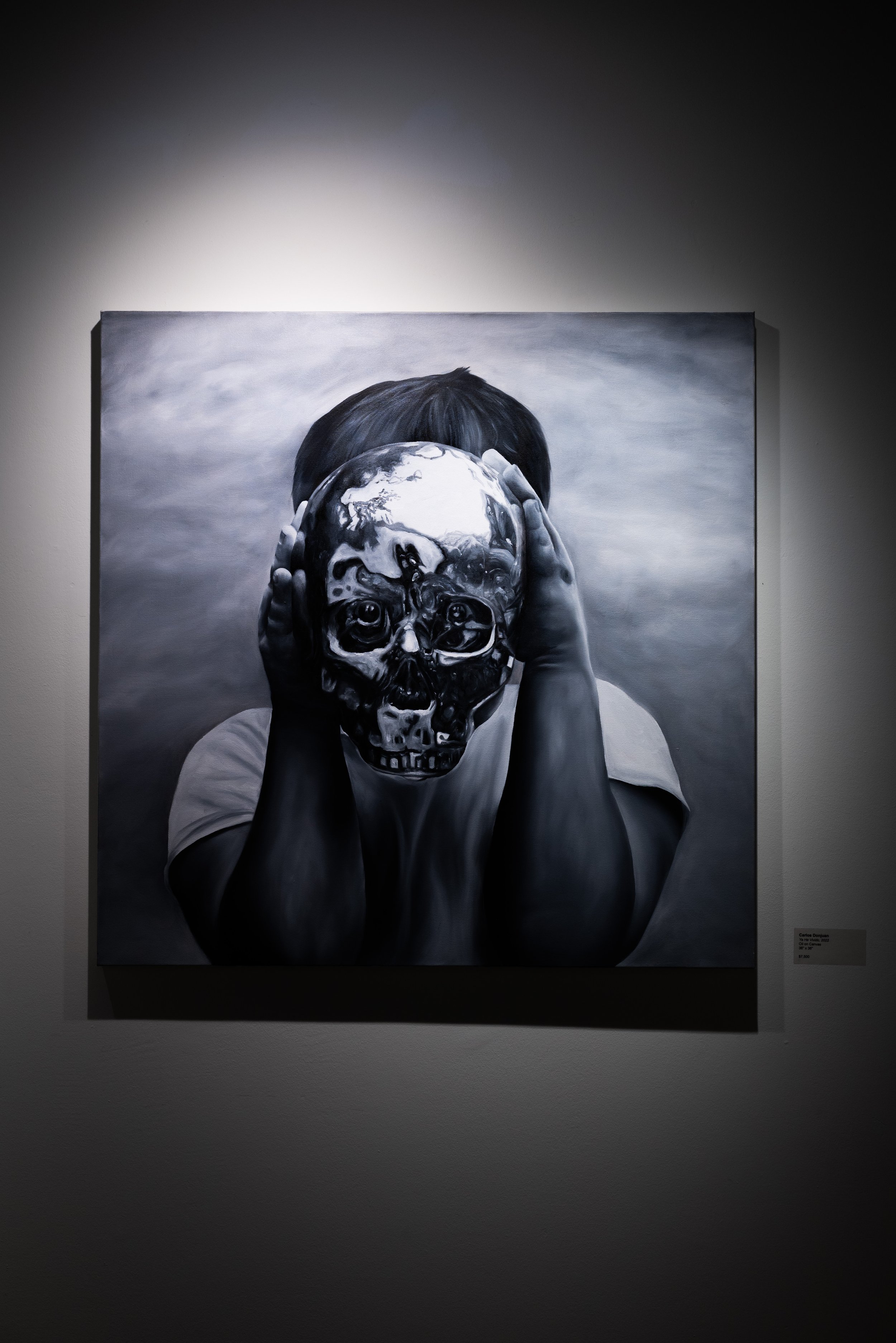 Child holding a reflective skull mask over their face in a black and white painting displayed on a gallery wall.