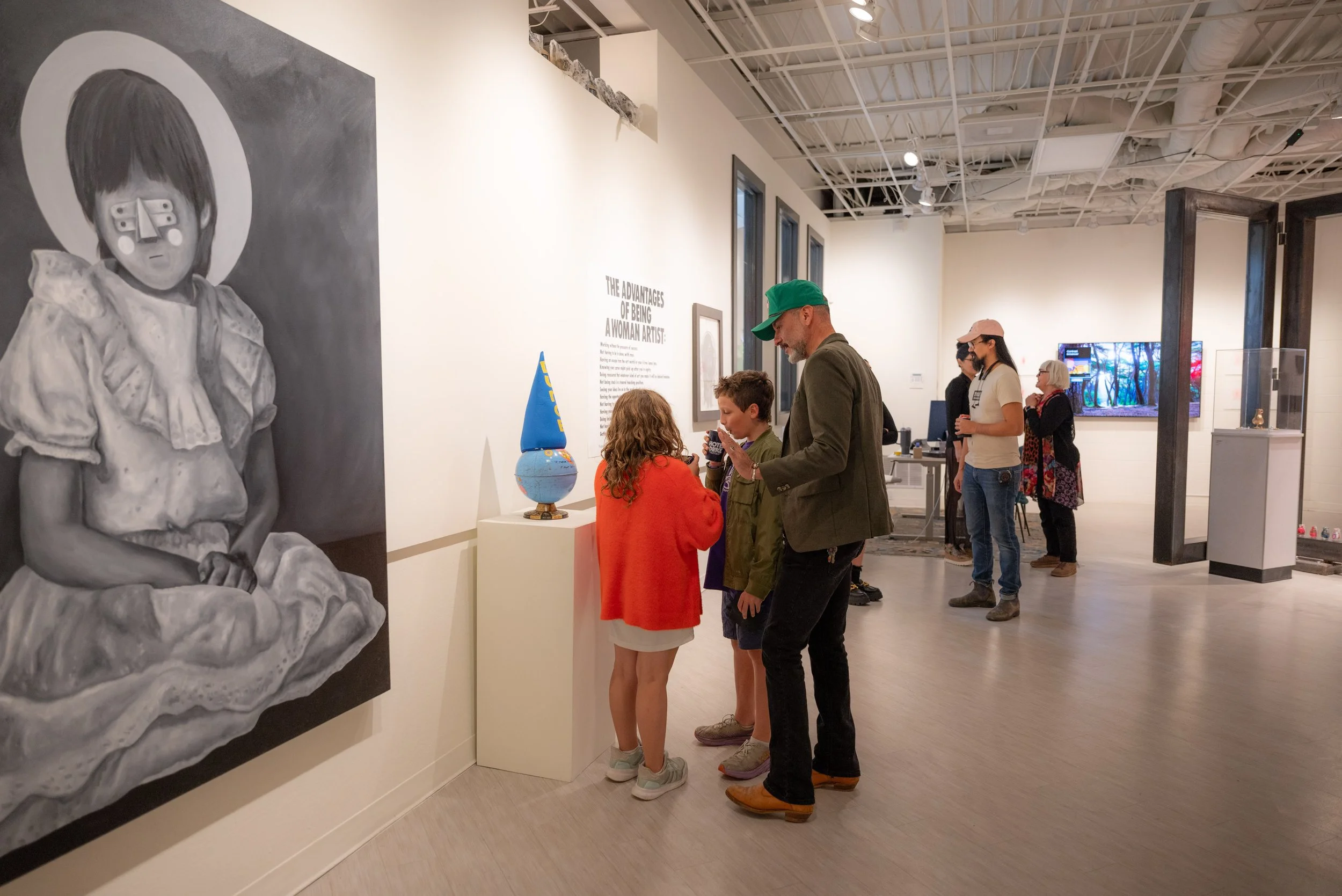 People viewing artworks and displays in a modern art gallery or museum with white walls and wooden floors.