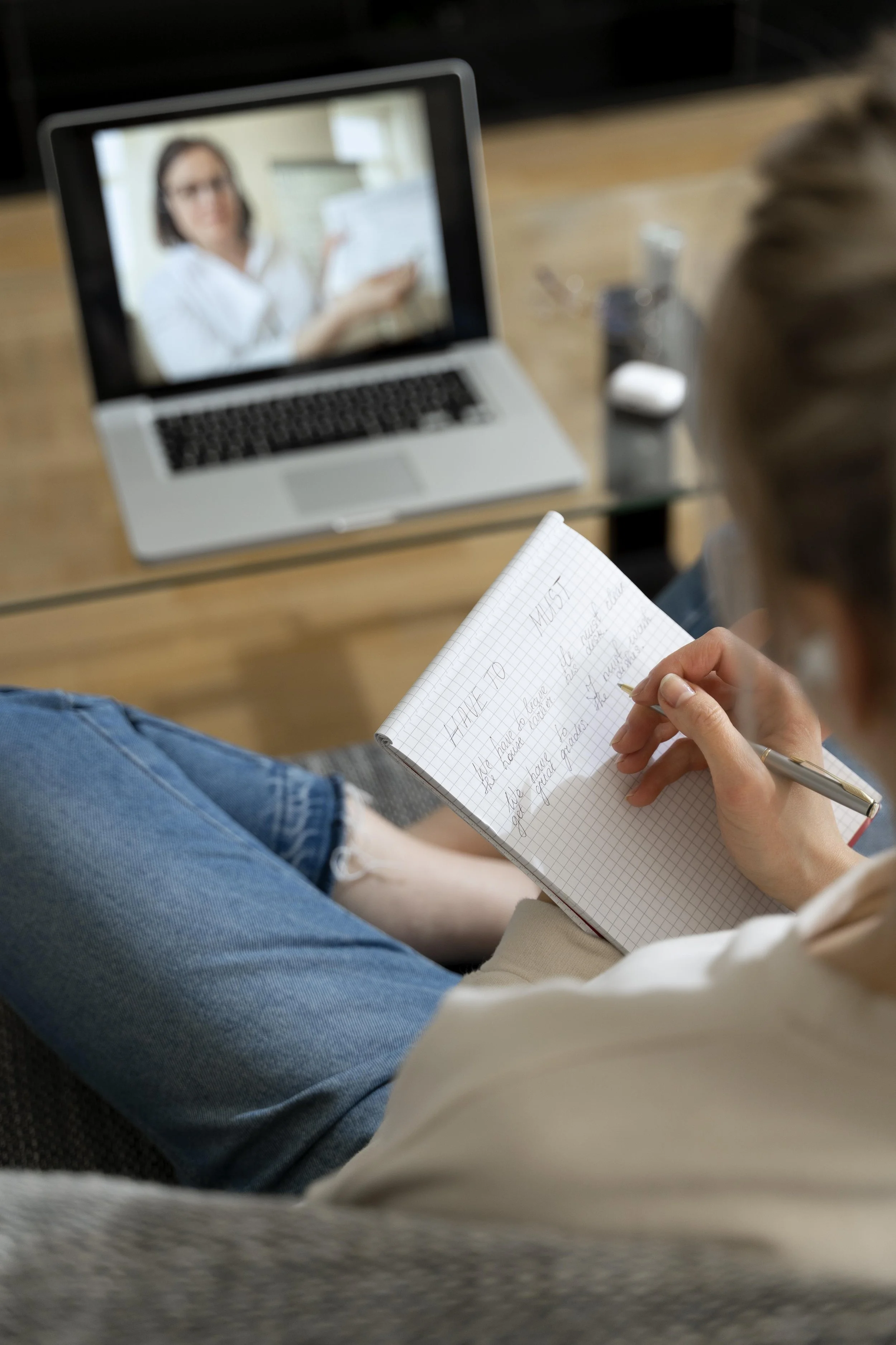Person taking notes while participating in a virtual meeting on a laptop.