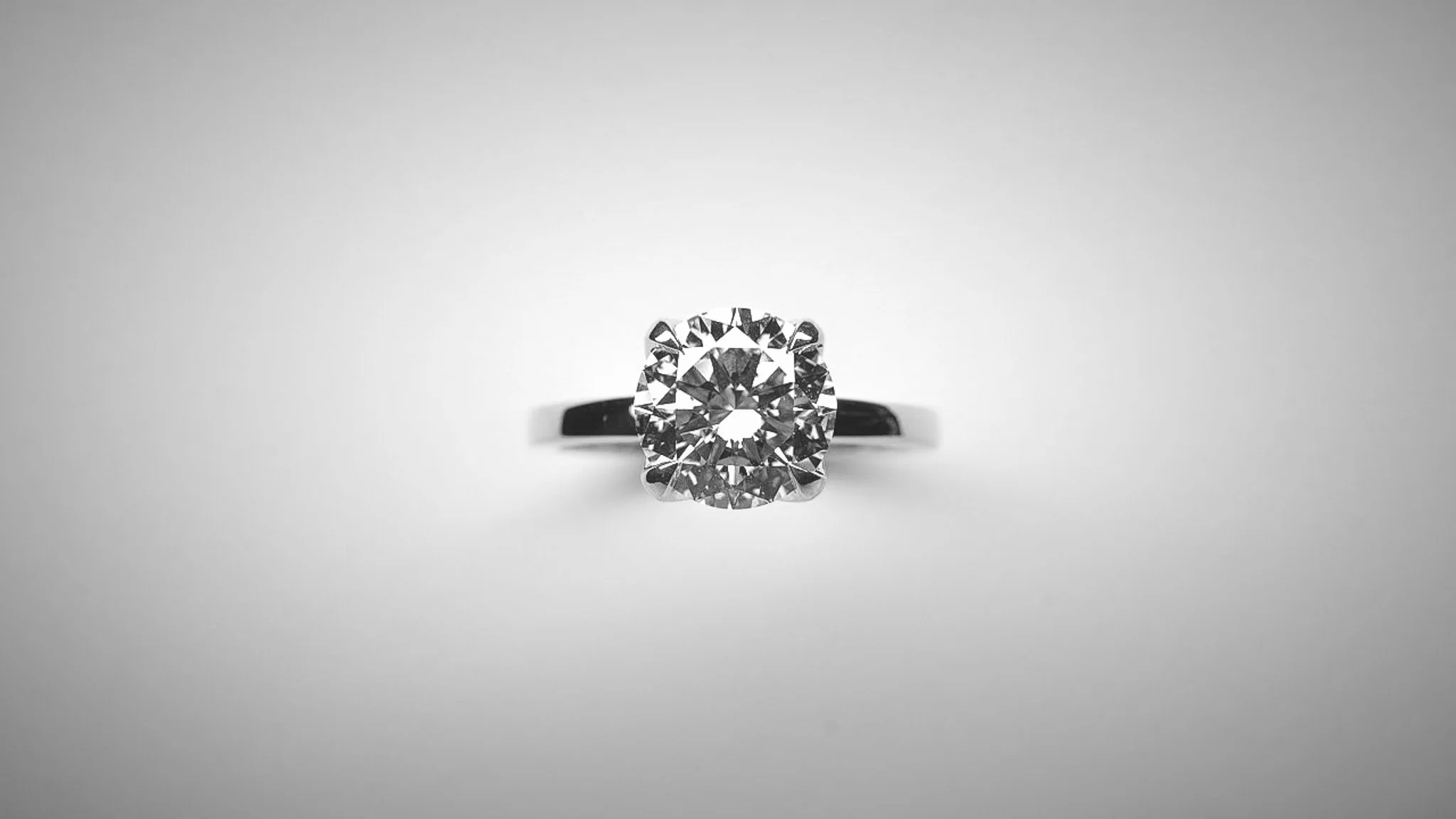 A close-up of a diamond engagement ring with a solitaire round-cut diamond on a gray background.