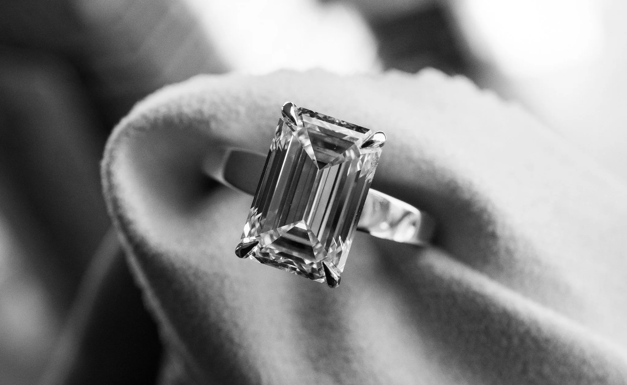 A large, rectangular emerald-cut diamond ring with a band, resting on a soft, textured fabric surface.