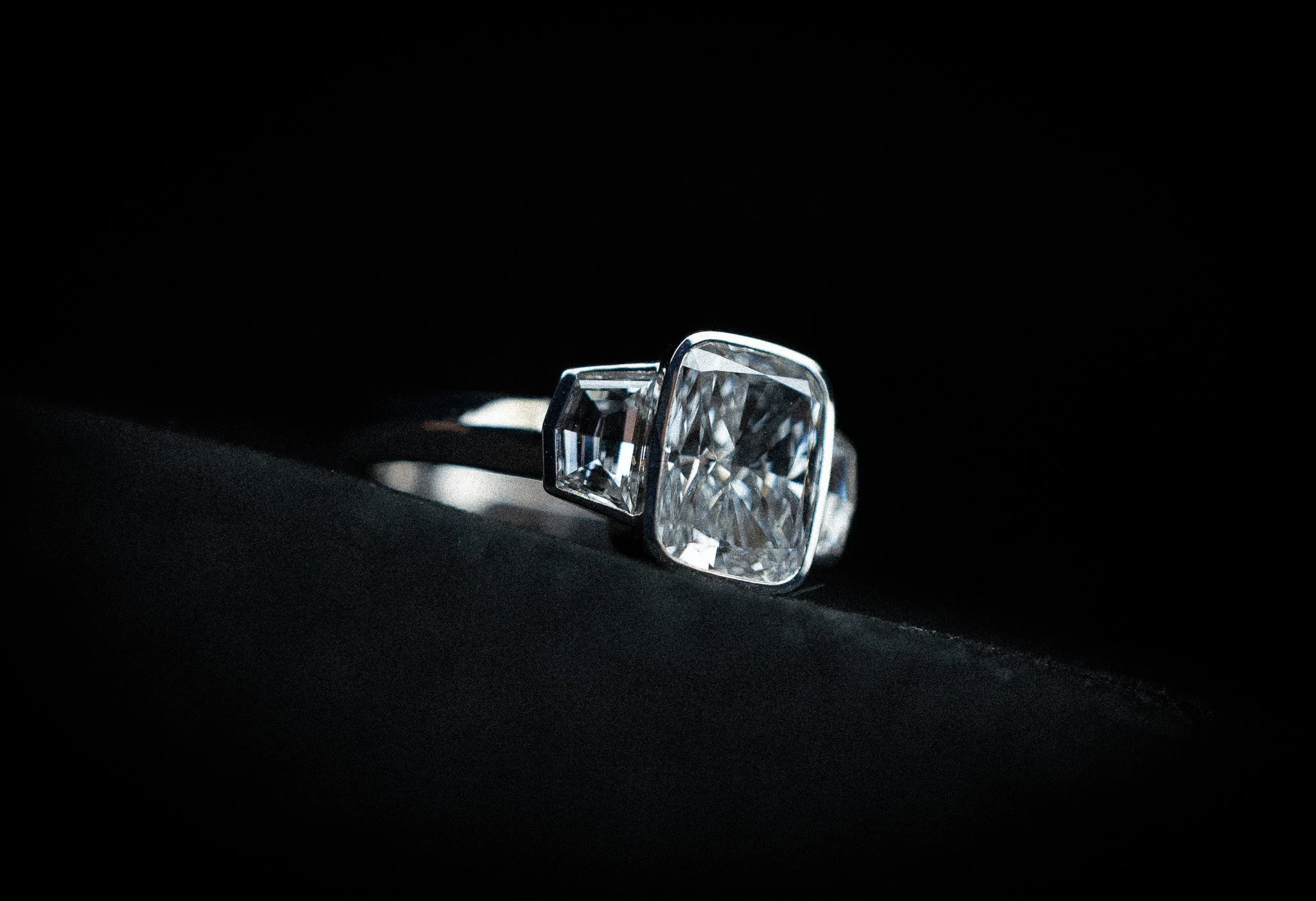 Close-up of a silver ring with a large, rectangular-cut diamond in a dark setting.