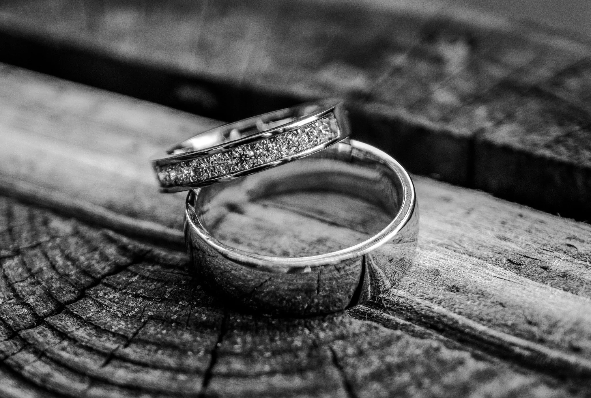 Close-up of two wedding rings, one with embedded diamonds, resting on a wooden surface in black and white.