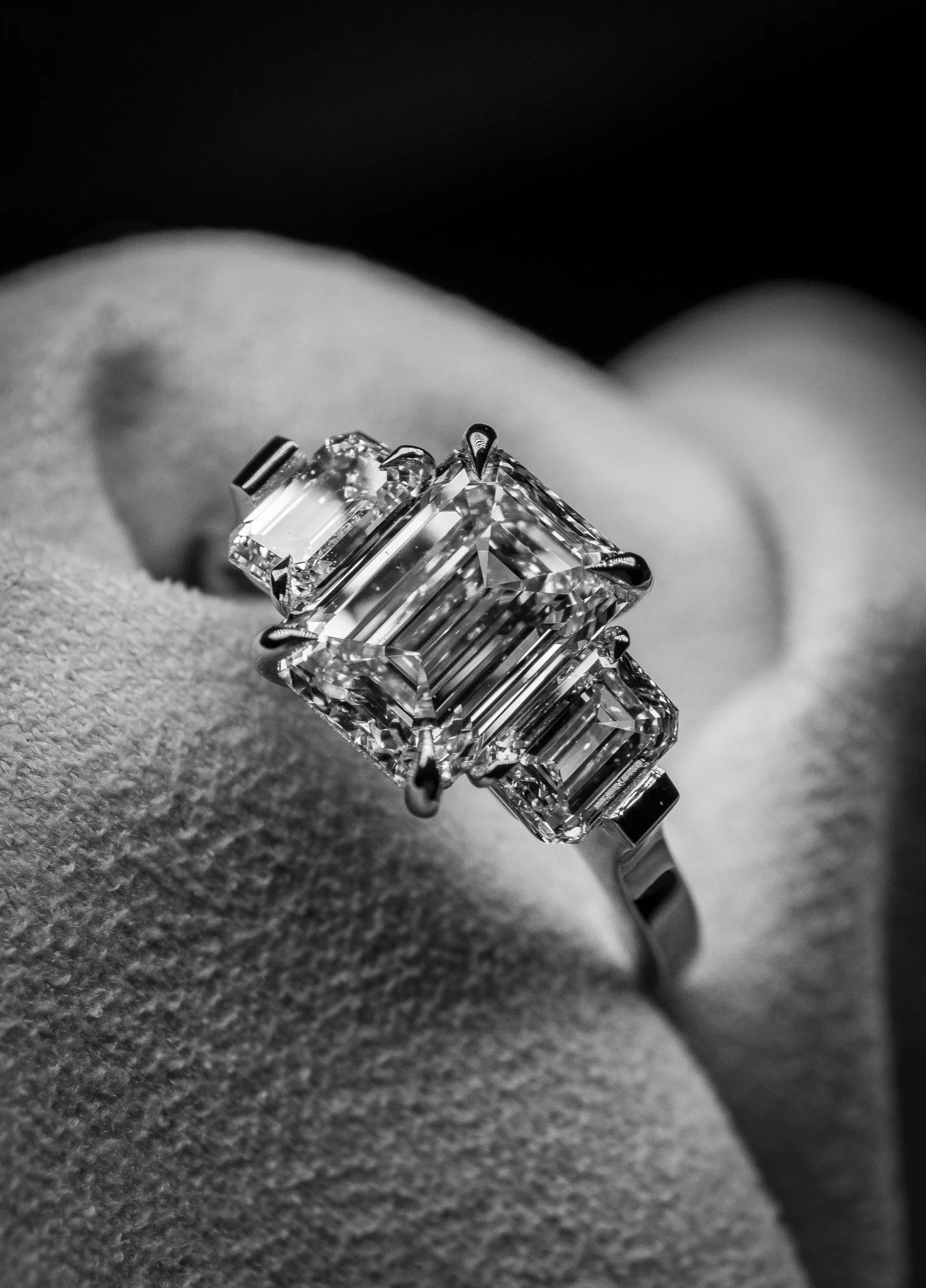 Close-up of a large, rectangular-cut diamond ring with multiple smaller diamonds, placed on someone's finger, in black and white.