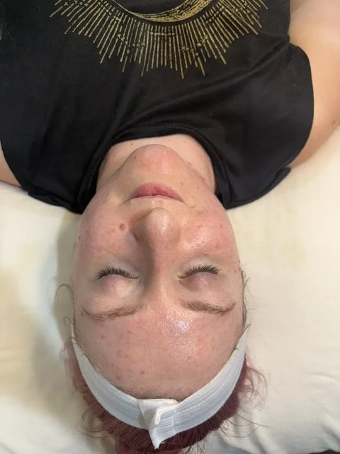 A woman lying down with eyes closed, wearing a white headband, and a black shirt with a gold sunburst design on it.