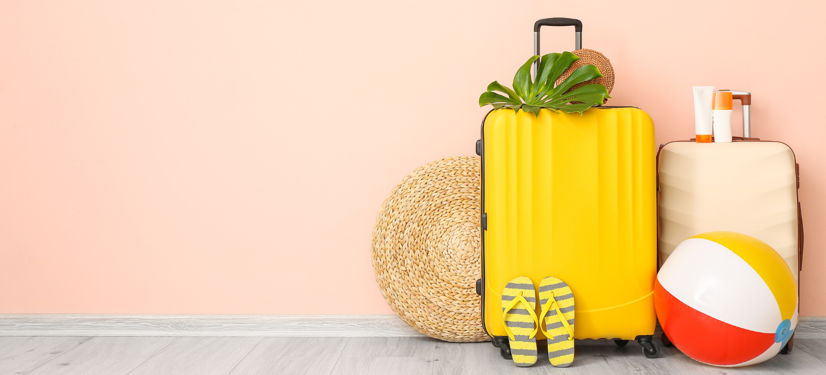suitcases, flip flops, a sun hat, and a beach ball are lined up against a peach wall