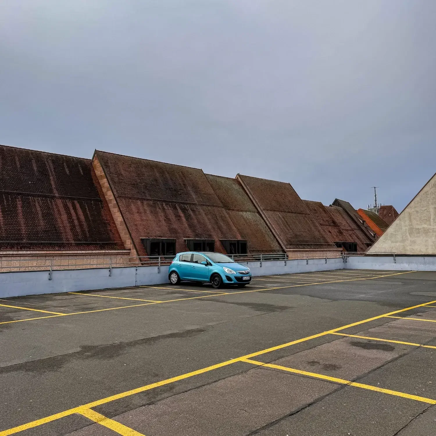 Parkplatz Adlerstraße in Nürnberg mit einem blauen Auto und vielen leeren Stellplätzen, Dächer im Hintergrund