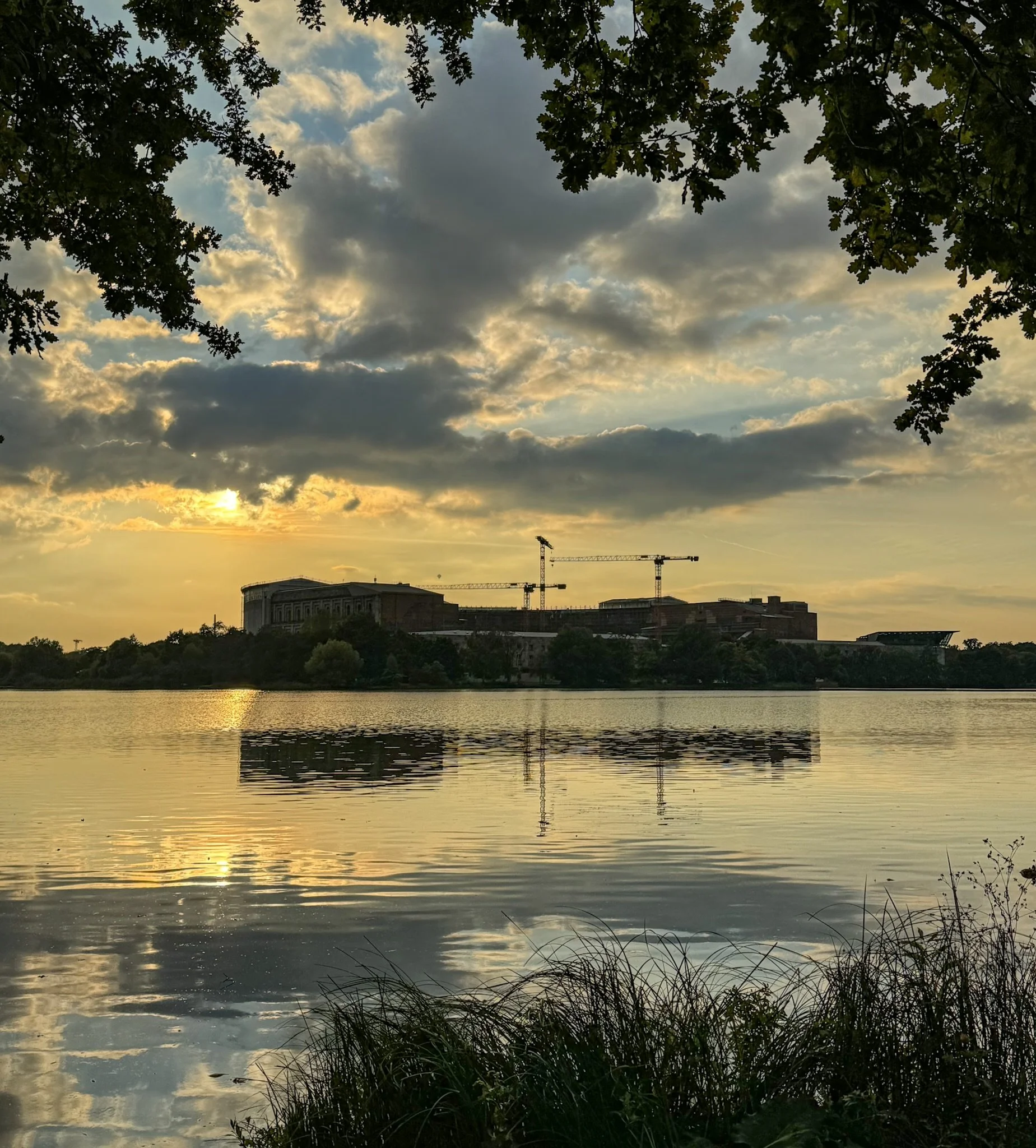 Sonnenuntergang am Dutzendteich Nürnberg mit Kongresshalle und Baustelle, dramatische Wolkenspiegelung im Wasser, Kräne im Hintergrund