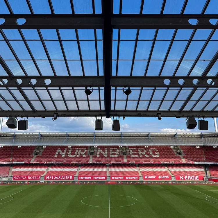 Innenansicht des Max-Morlock-Stadions in Nürnberg mit Blick auf das Spielfeld, die roten Tribünen mit dem Schriftzug "NÜRNBERG" und das Glasdach. Das Stadion ist nach dem Spiel vom Club gegen Kiel (0:3) menschenleer.
