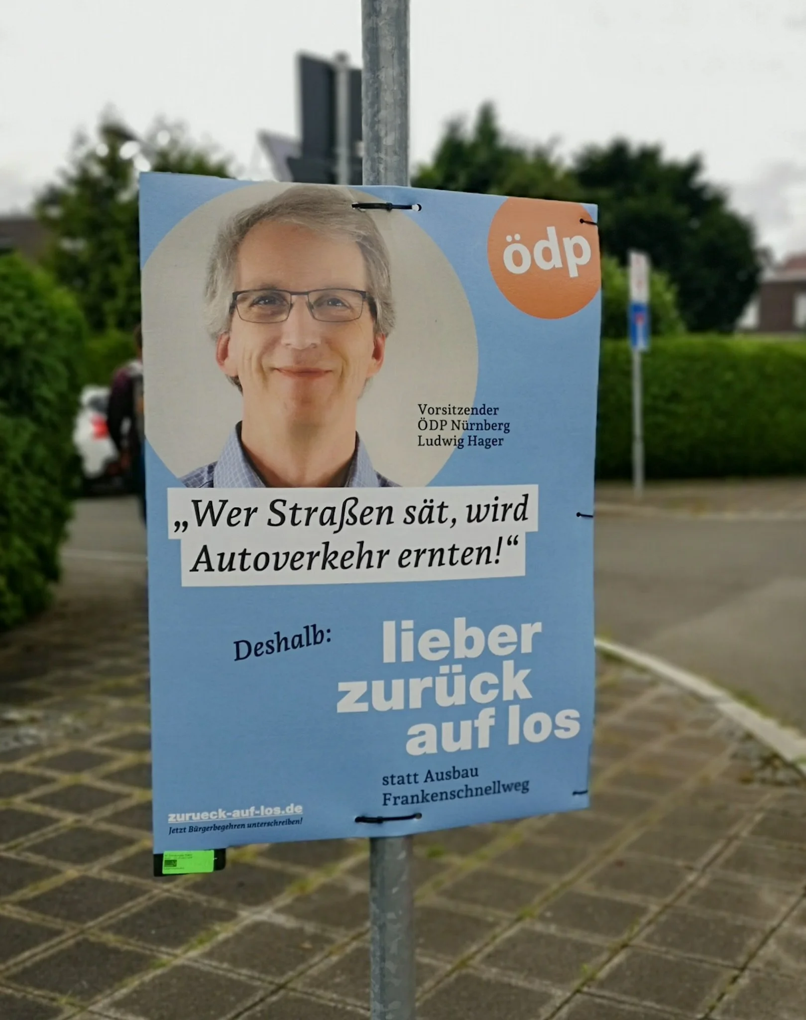  ÖDP-Politiker auf Wahlplakat mit Slogan "Wer Straßen sät, wird Autoverkehr ernten! Deshalb: lieber zurück auf los" 