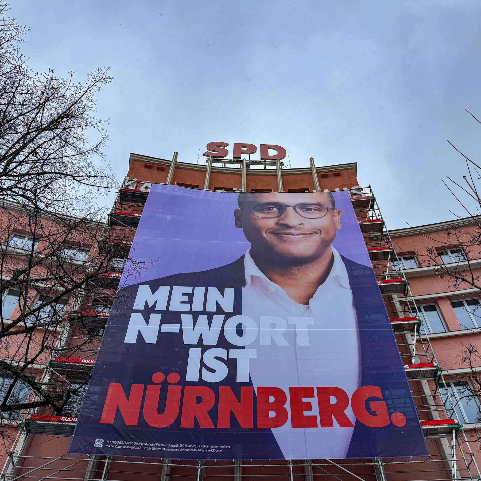 Fassadenfüllendes Wahlplakat von Nasser Ahmed am Karl-Bröger-Haus in Nürnberg mit der Aufschrift: ‚Mein N-Wort ist Nürnberg‘ vor bewölktem Himmel