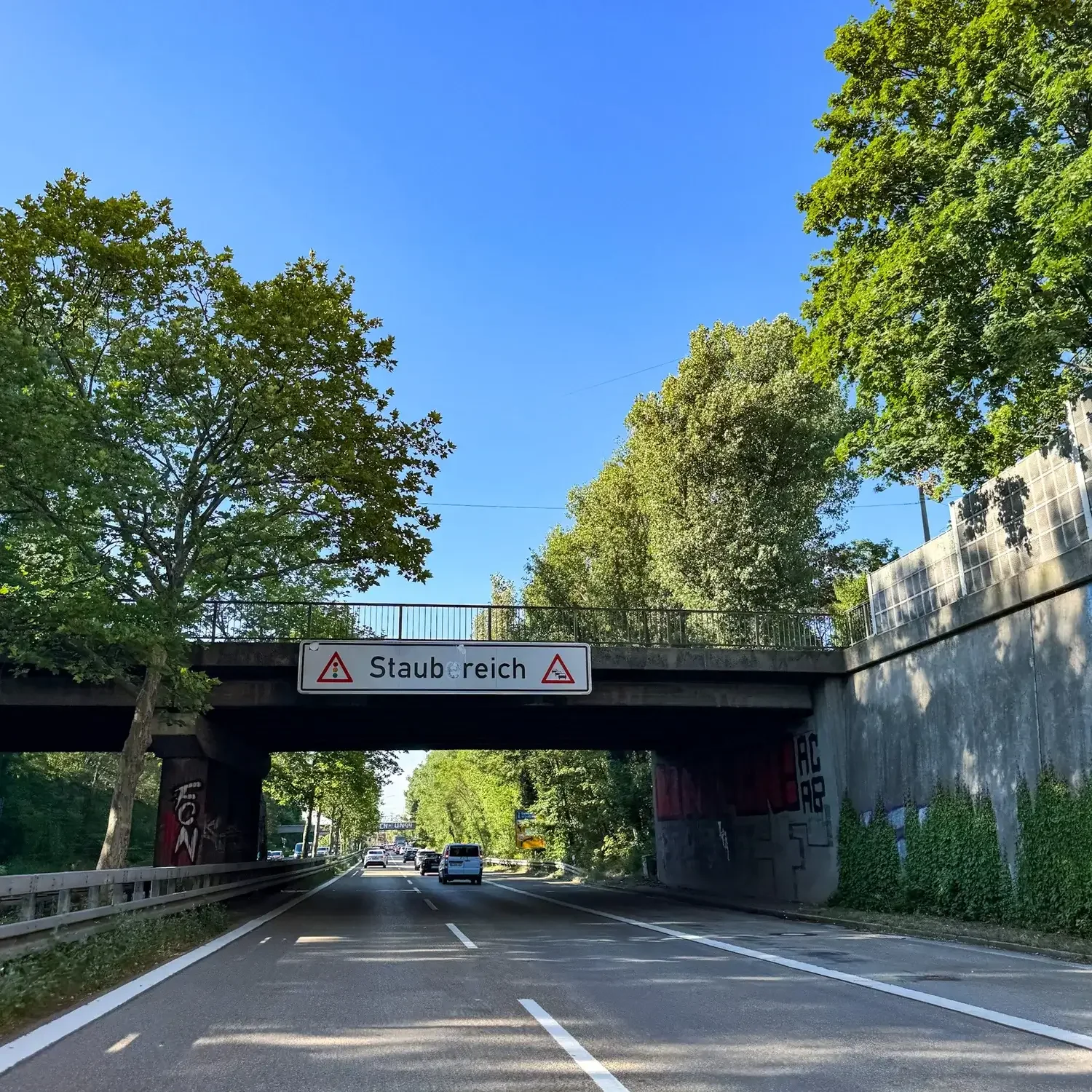 Stauwarnschild an einer Brücke über dem Frankenschnellweg in Nürnberg, Schriftzug teils übermalt, darunter Verkehr. Juli 2026