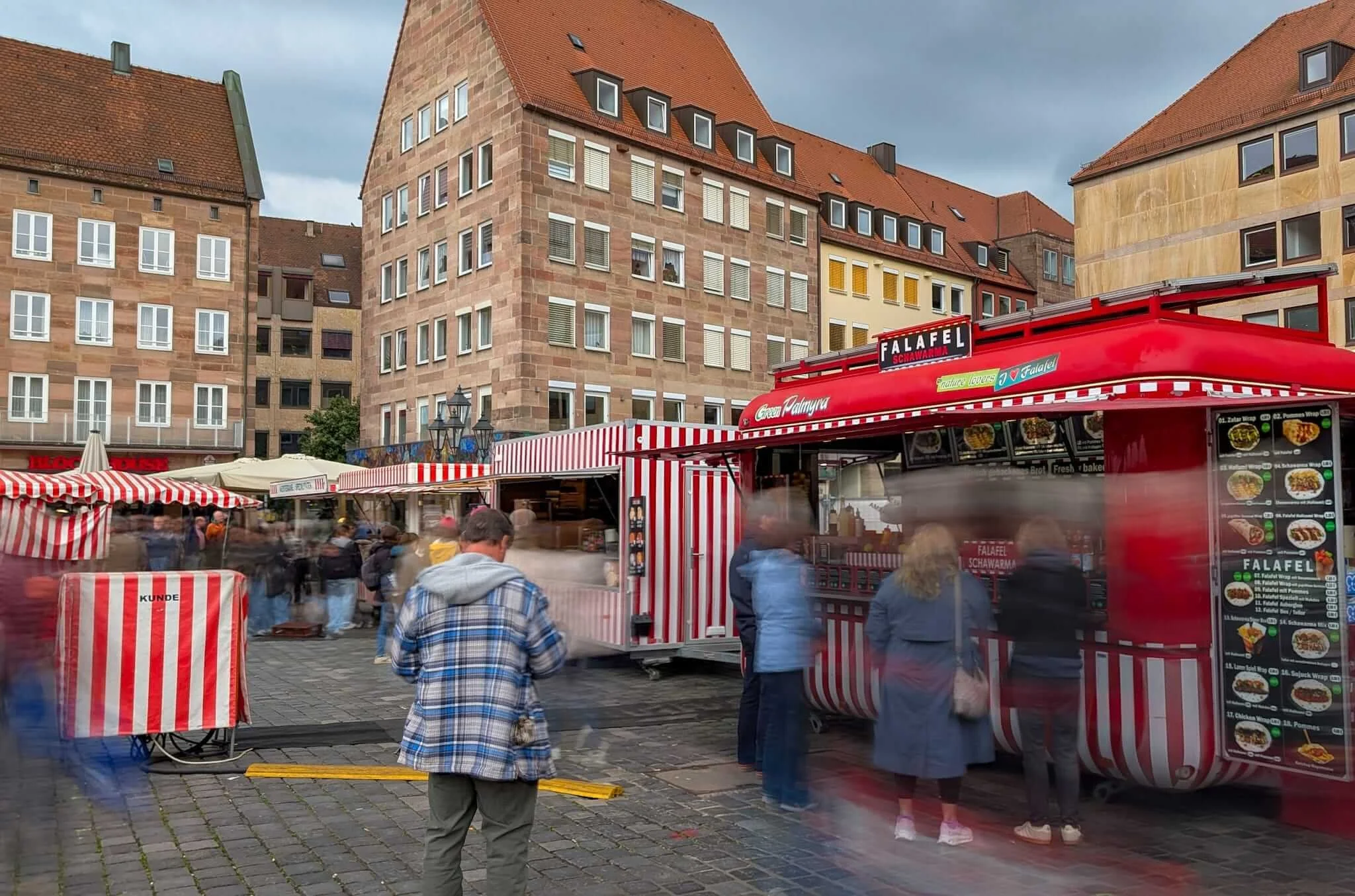 Ein roter Foodtruck mit der Aufschrift Falafel auf dem Nürnberger Hauptmarkt. Durch eine Langzeitbelichtung verschwimmen die vorbeilaufenden Passanten zu unscharfen Schemen.