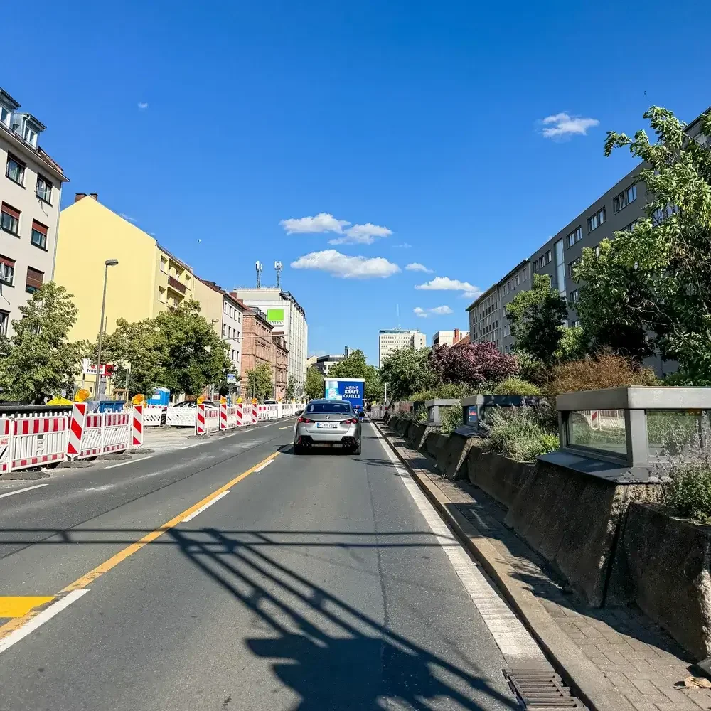 Foto der Fürther Straße in Nürnberg im aktuellen, stark befahrenen Zustand mit Betonbarrieren, Baustellenbaken und fließendem Verkehr als Beleg für die fehlende Boulevardqualität vor dem Bürgerentscheid.
