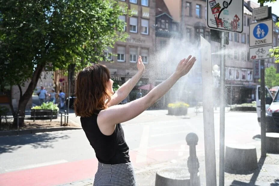 Eine Frau hält ihre Arme in den Wassernebel einer Sprühnebelsäule in der Königstraße in Nürnberg.