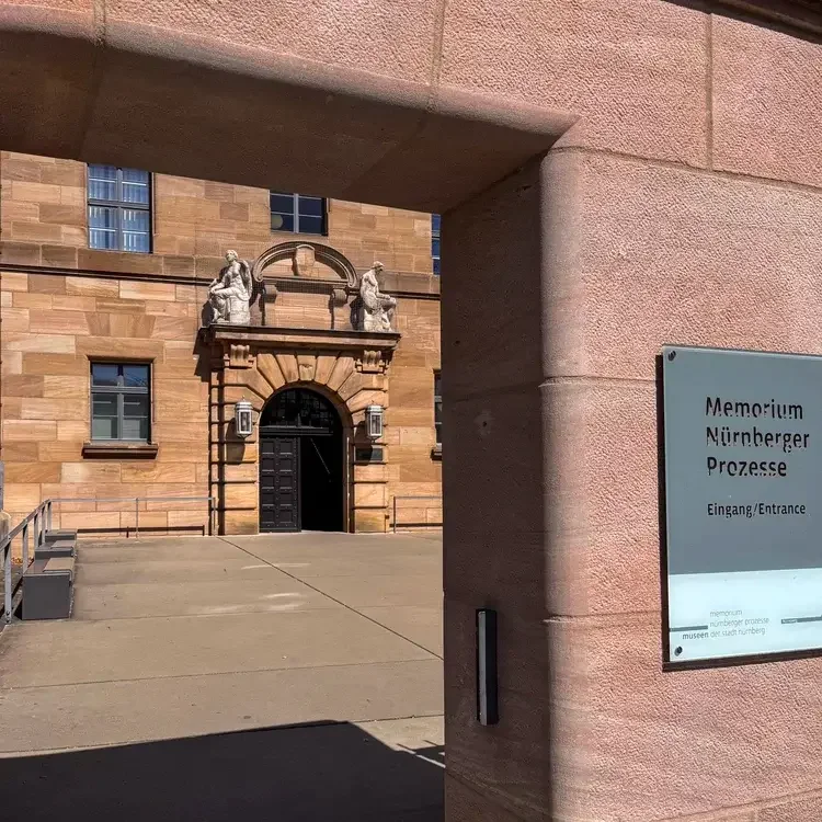Eingang zum Memorium Nürnberger Prozesse mit Hinweisschild, Blick durch moderne Architektur auf historisches Gerichtsgebäude