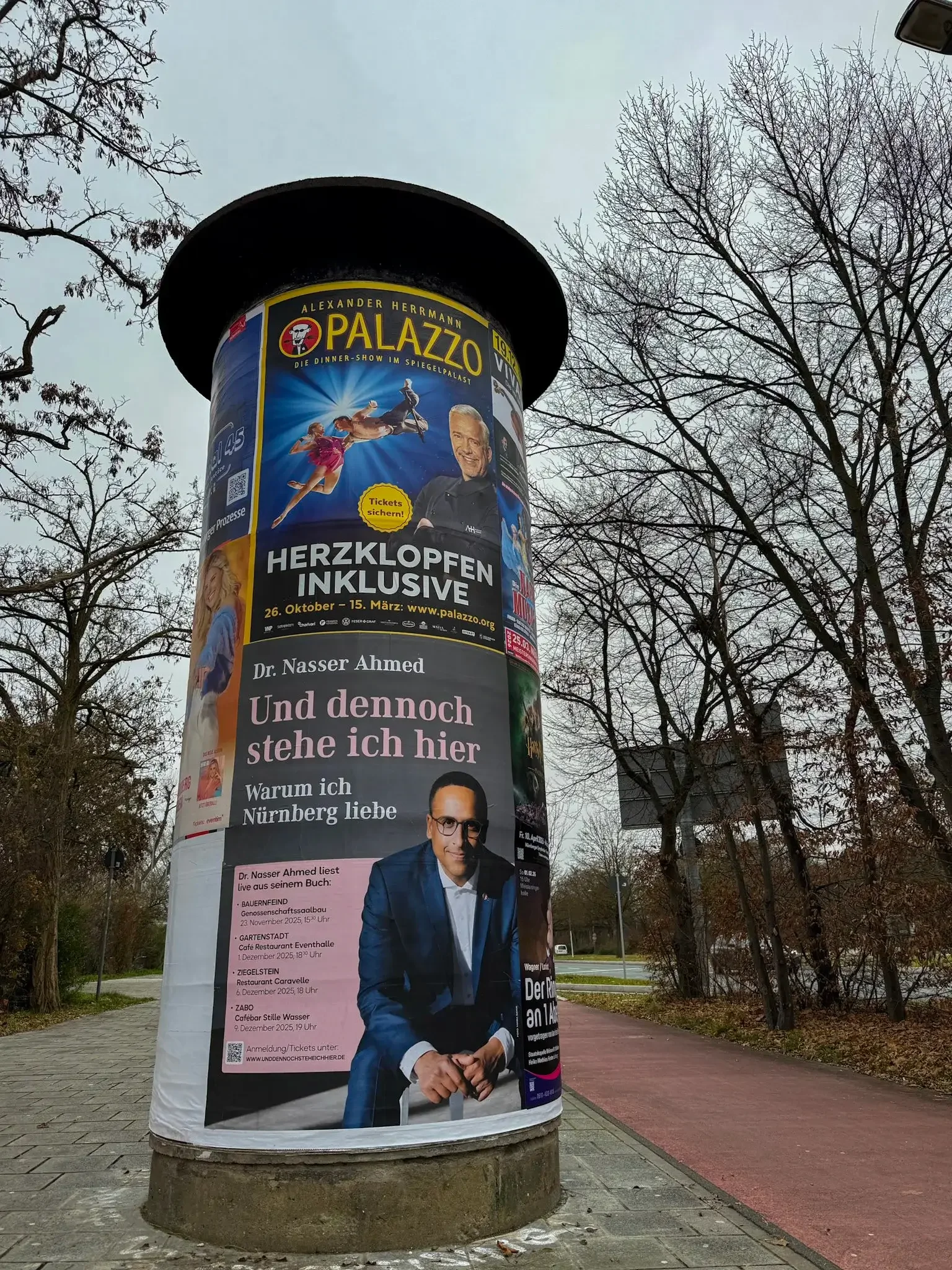SPD-Oberbürgermeisterkandidat Nasser Ahmed auf Litfaßsäule in Nürnberg mit Slogan "Und dennoch stehe ich hier" – sitzt aber auf einem Stuhl
