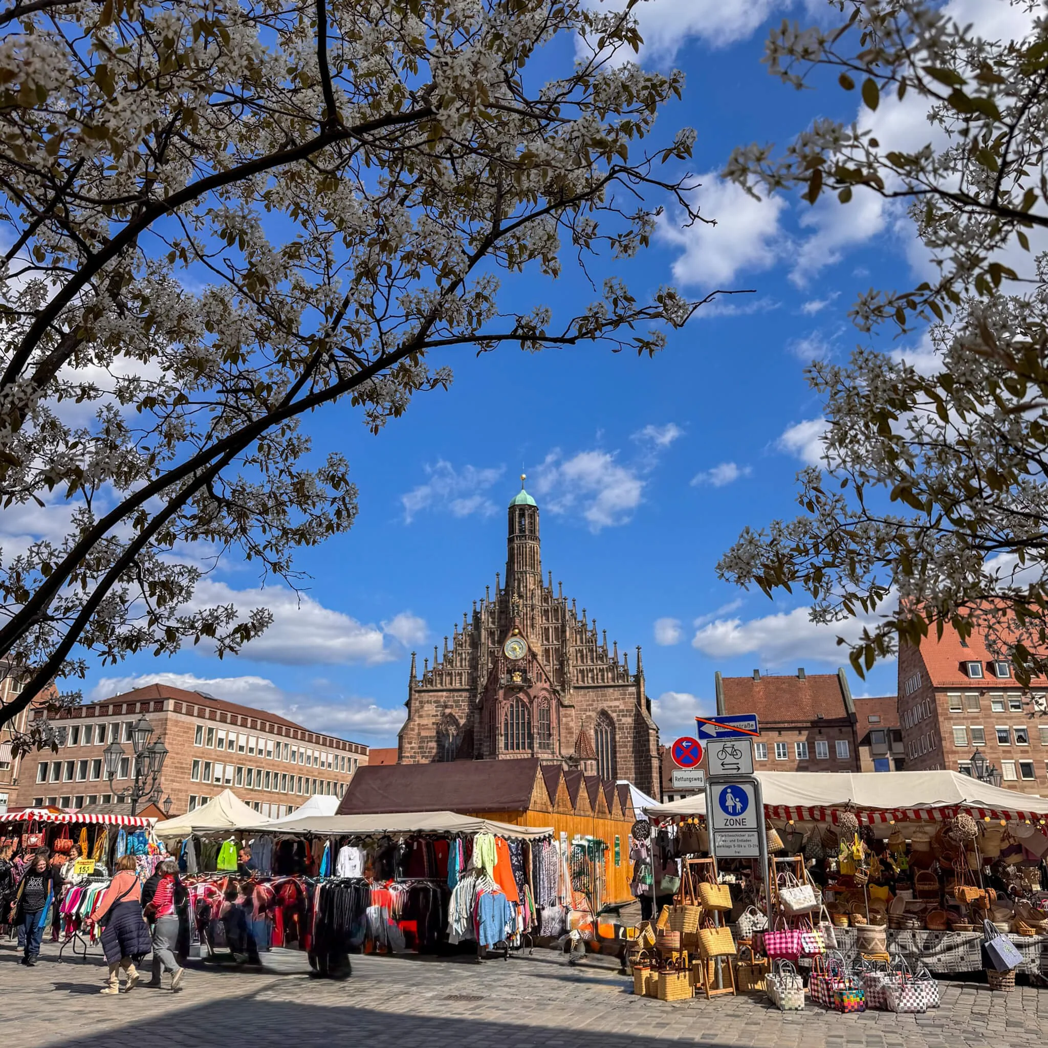 Blick über den Nürnberger Hauptmarkt mit Marktständen und der Frauenkirche unter blauem Himmel.