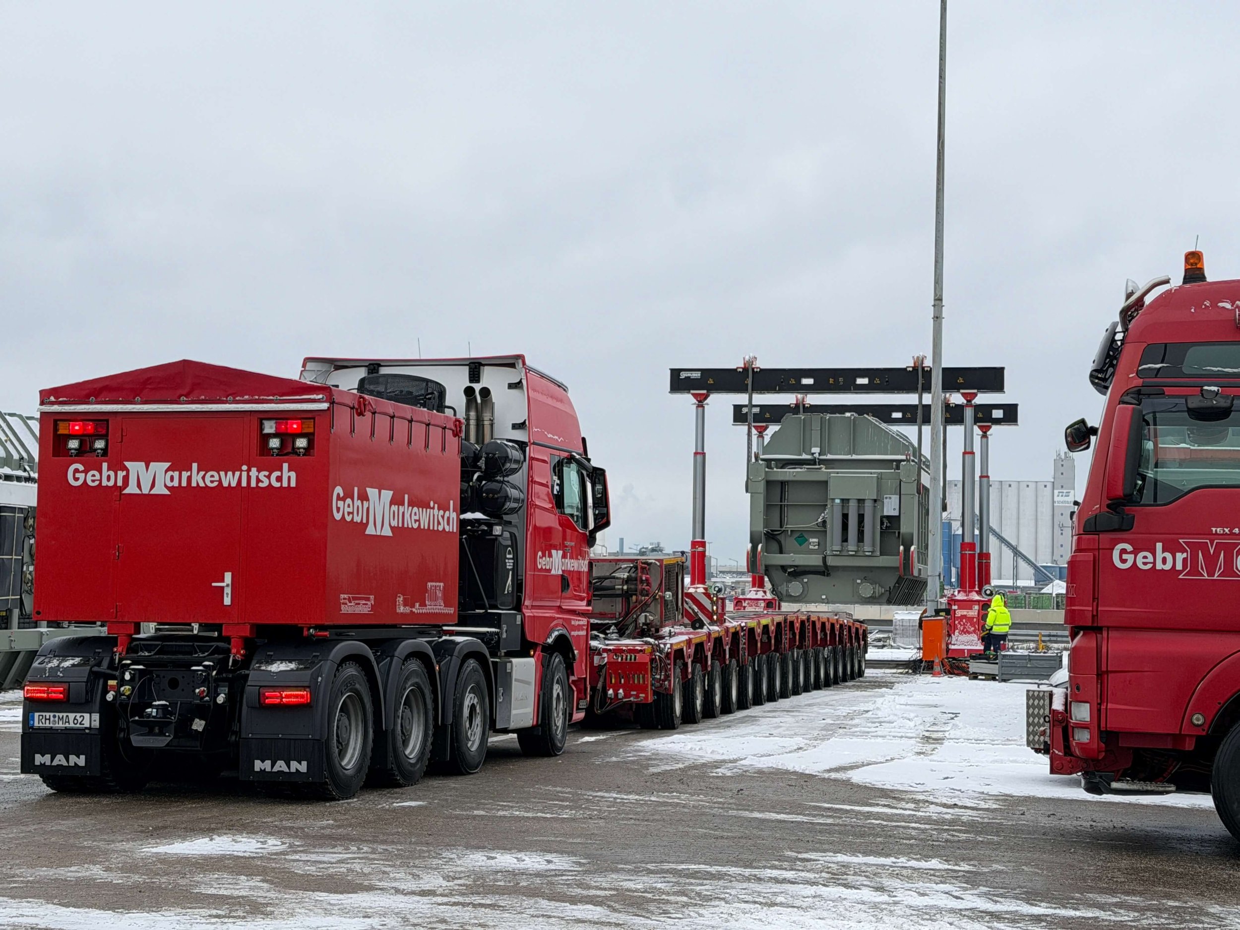 Ein roter Lastwagen der Spedition Markewitsch transportiert eine massive Industrieanlage im verschneiten Hafen Nürnberg.