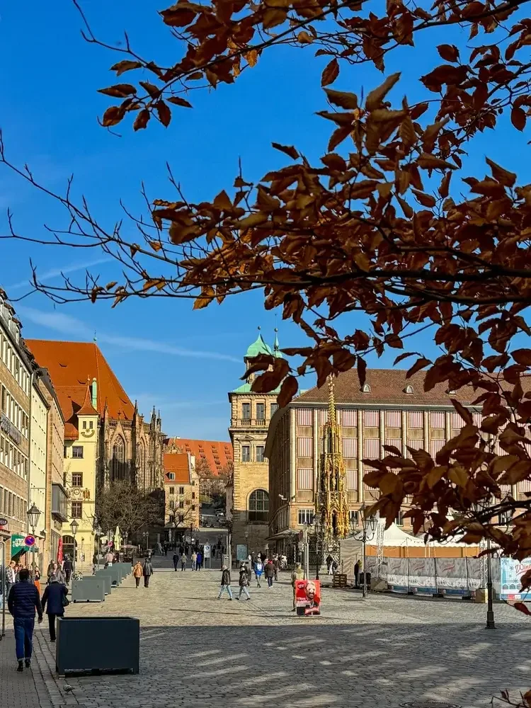 Leere dunkelgraue Pflanzkübel stehen auf dem gepflasterten Nürnberger Hauptmarkt bereit für die neuen mobilen Bäume. Im Hintergrund sind der Schöne Brunnen, St. Sebald und das alte Rathaus zu sehen