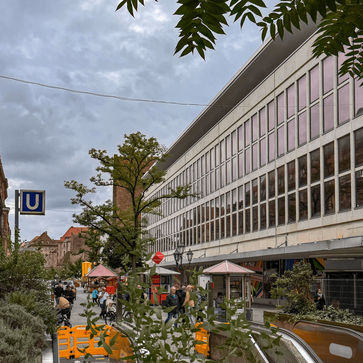 Fassade des ehemaligen Kaufhofs an der Königstraße in Nürnberg, davor Verkaufsstände, Passanten und ein versperrter U-Bahn-Zugang.