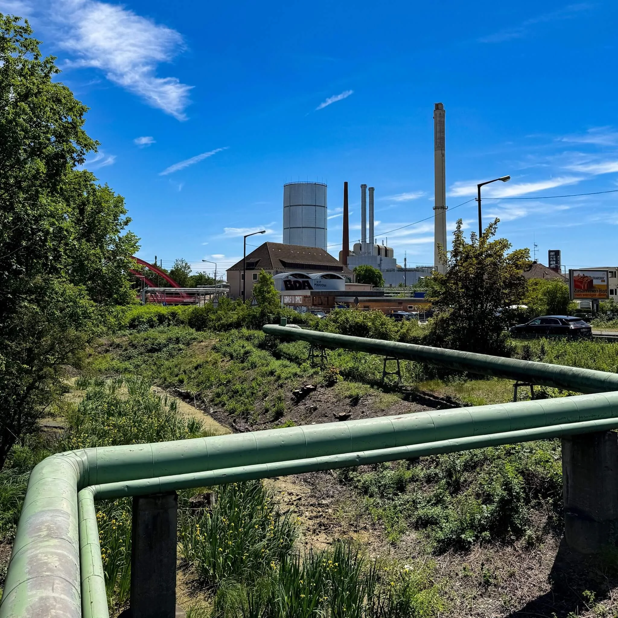 Fernwärmerohre im Vordergrund, dahinter das N-ERGIE Heizkraftwerk Sandreuth in Nürnberg bei Tageslicht