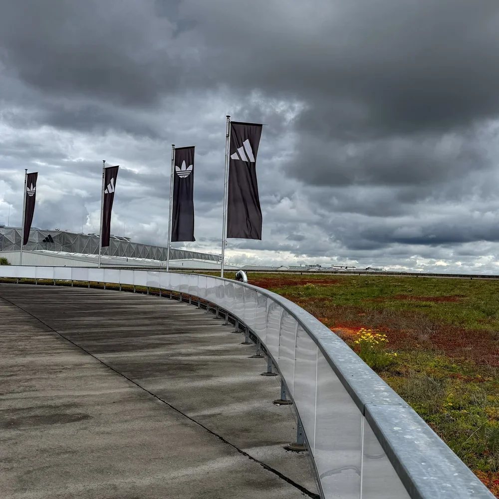 Schwarze Adidas-Fahnen wehen unter einem dunklen, bewölkten Himmel über dem Firmengelände