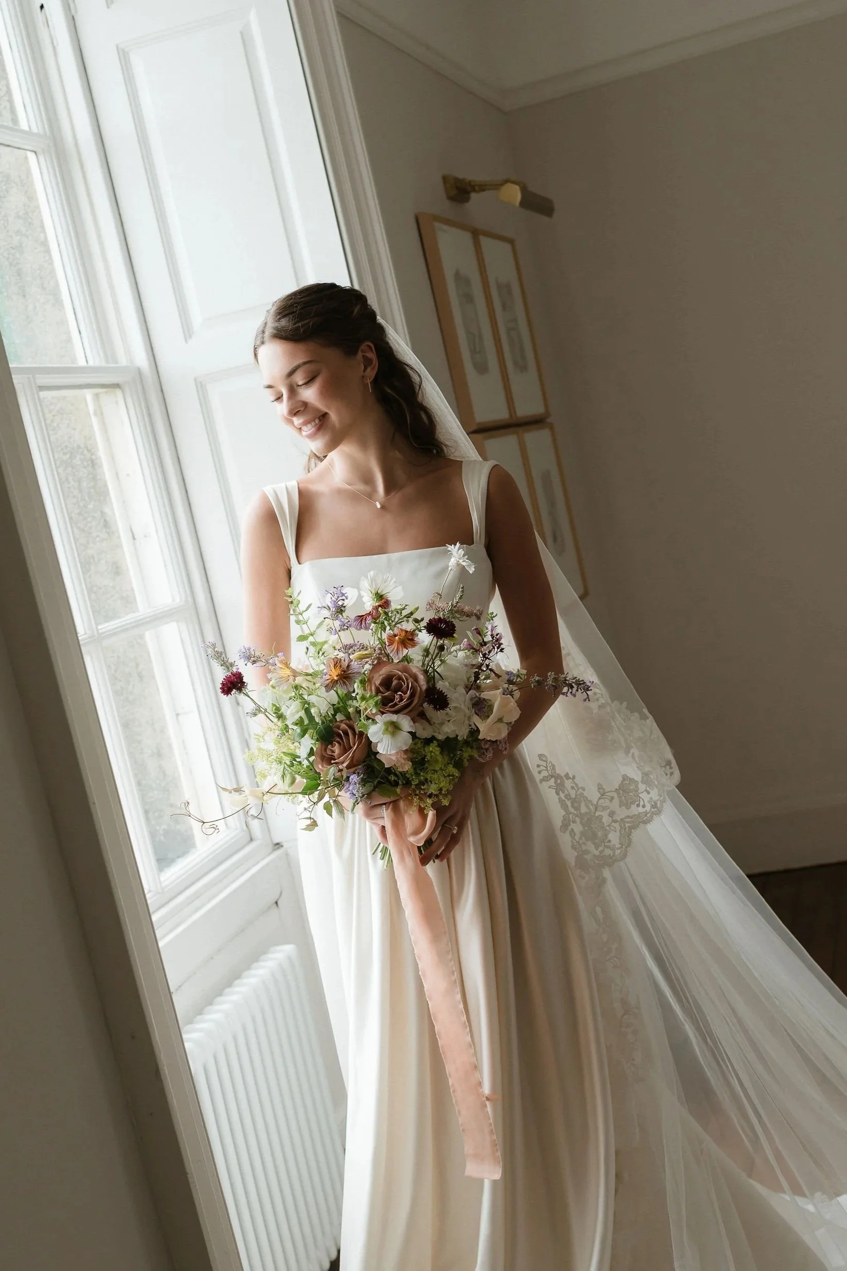 A bride holding her seasonal, earthy coloured bridal bouquet at Forcett Hall in Yorkshire
