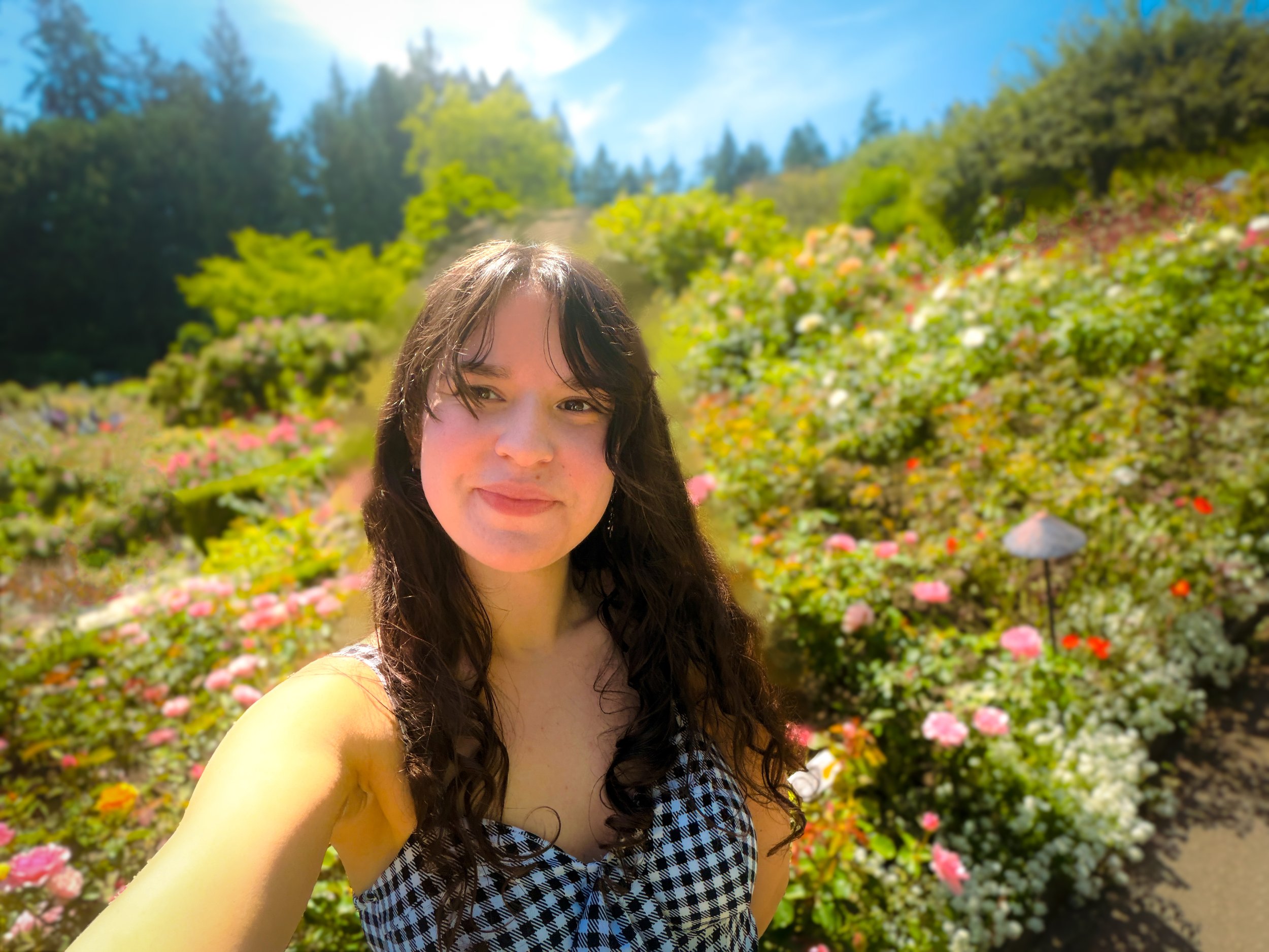 Illustrator and artist Juliet Roselie smiling in a colorful, sunlit garden surrounded by flowers and greenery