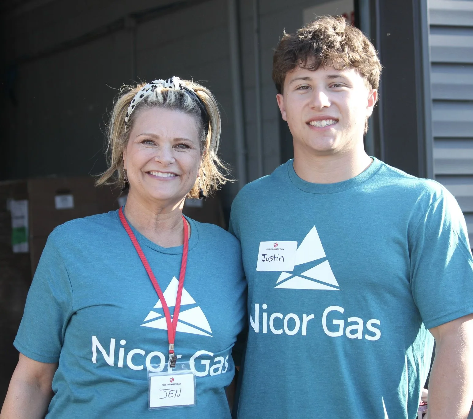 Two smiling Nicor Gas volunteers, a woman and a man in matching blue company shirts, standing outside the Food for Greater Elgin pantry.