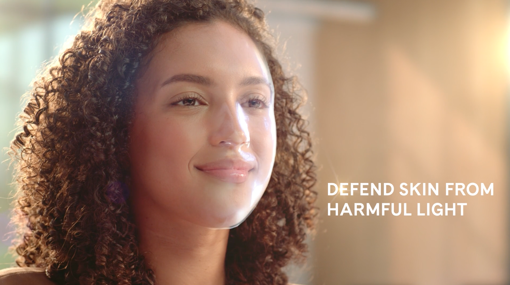 Profile shot of a smiling woman with curly hair looking off-camera into bright natural sunlight.