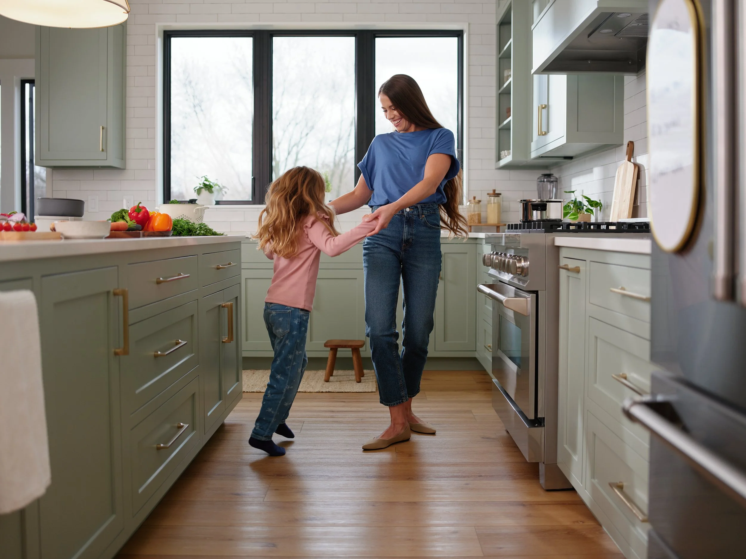 Mother and daughter dancing in the kitchen, representing a joyful health and wellbeing lifestyle.